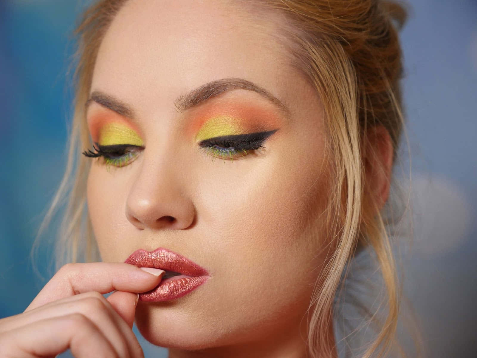 Spring Makeup 桌布 壁紙 — 一個特寫肖像，一位女性帶有鮮明的黃色和橙色眼影以及金屬粉紅色的嘴唇，背景是柔和的藍色。