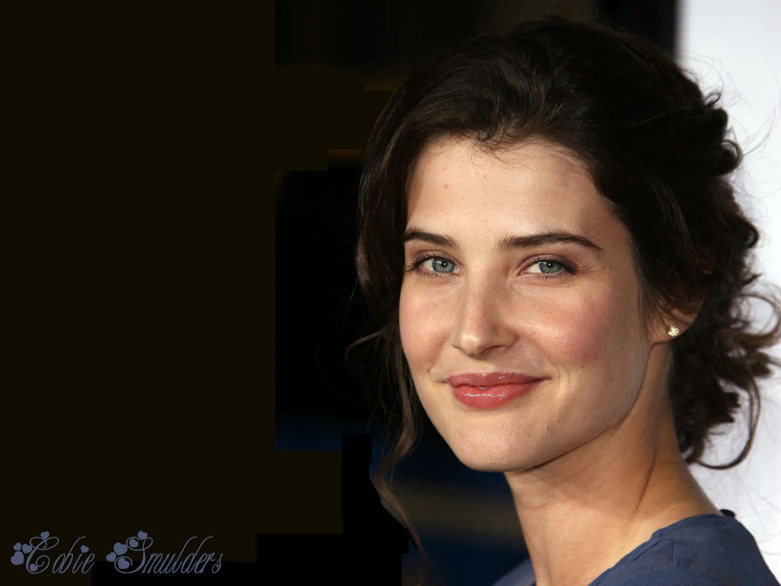 Cobie Smulders 桌布 壁紙 — 一個特寫肖像，一位擁有深色波浪頭髮和藍色眼睛的女性在深色背景下溫柔微笑。