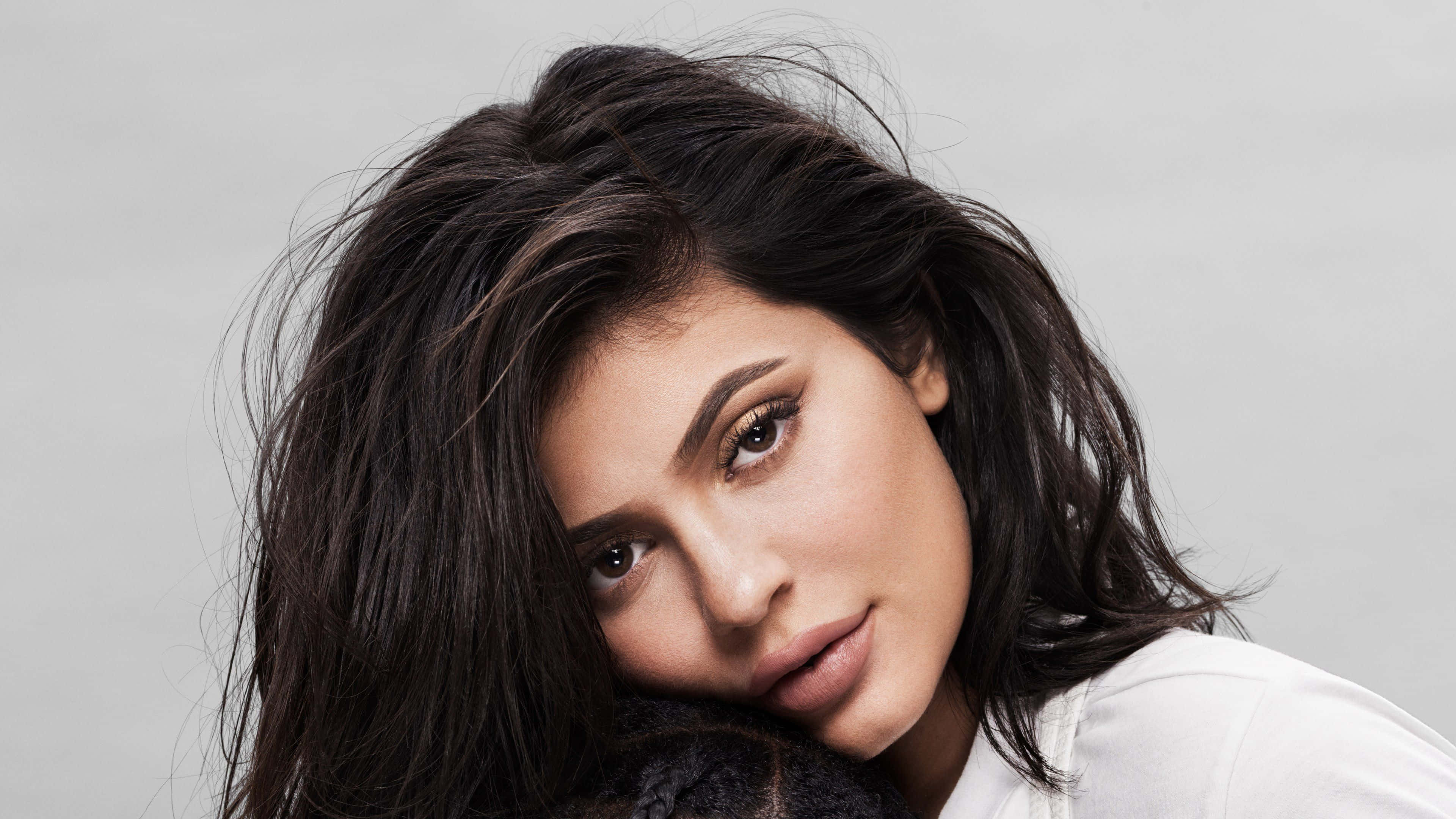 Kylie Jenner 桌布 壁紙 — 一個特寫肖像，一位深色凌亂頭髮的女性在純灰色背景下直視鏡頭。