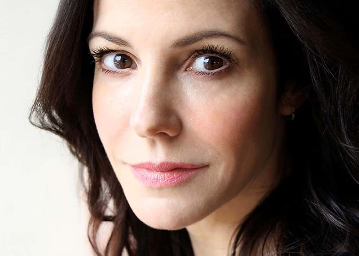 mary louise parker 桌布 壁紙 — 一個特寫肖像，一位深色頭髮和溫暖棕色眼睛的女性在純色背景前柔和地凝視相機。