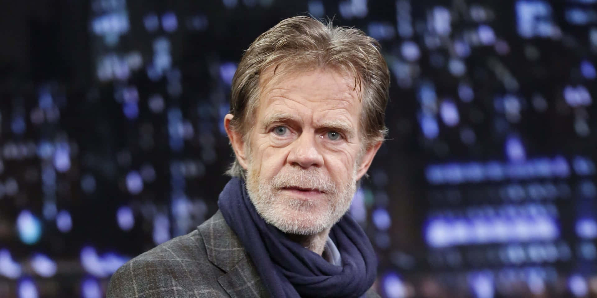 william h. macy 桌布 壁紙 — 一個特寫肖像，一名灰髮鬍鬚男子戴著深色圍巾，背景是模糊的城市燈光。