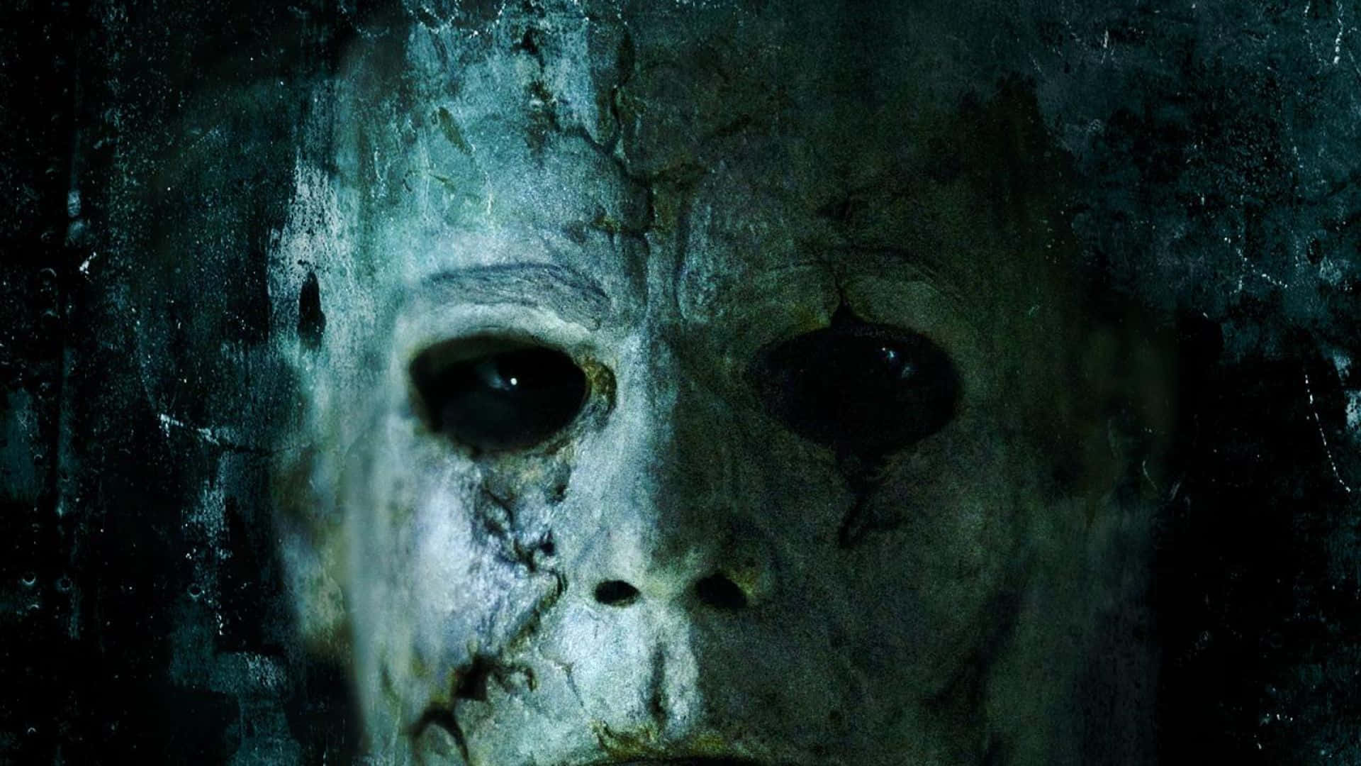 Mike Myers 桌布 壁紙 — 一個特寫鏡頭，展示一個風化的白色面具，帶有裂紋質感和黑色眼孔，背景是粗糙的深色。