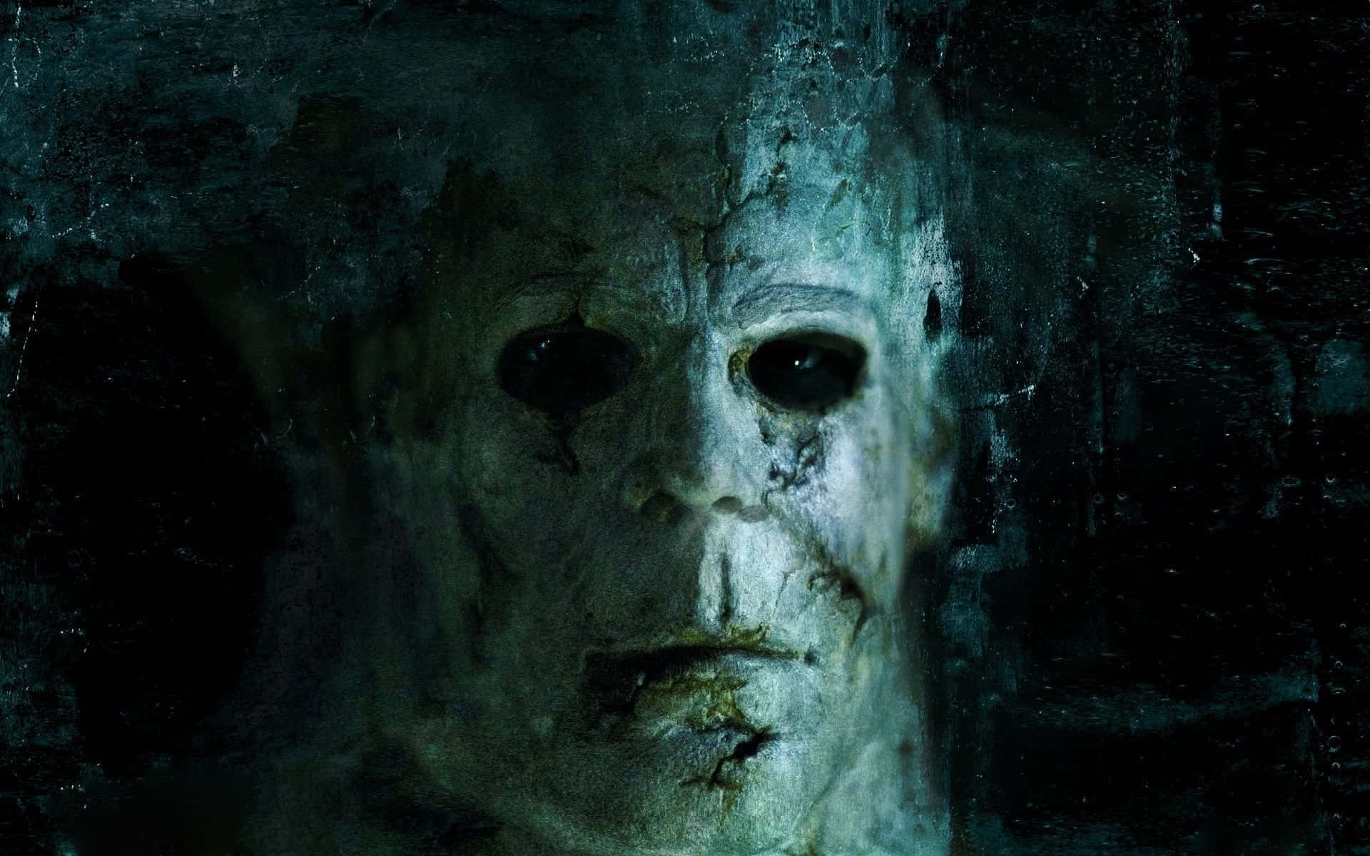 米高邁亞斯 桌布 壁紙 — 一個特寫鏡頭，展示一個風化的白色面具，帶有裂紋油漆和黑色眼睛，置於粗糙的深色背景上。