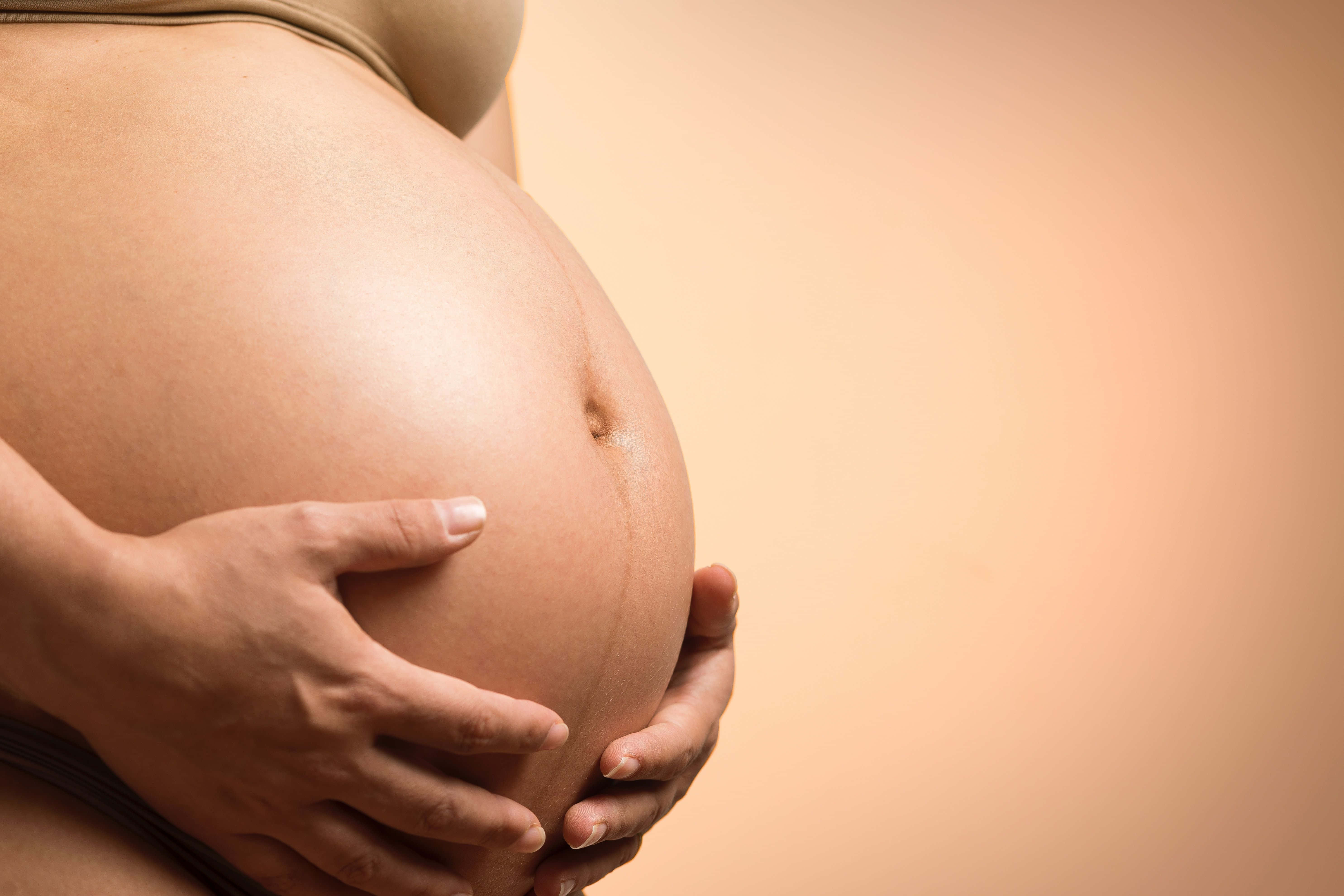 pregnancy 桌布 壁紙 — 一個特寫鏡頭，展示一雙手掌輕柔地托著孕婦的肚子，背景是柔和的蜜桃色。
