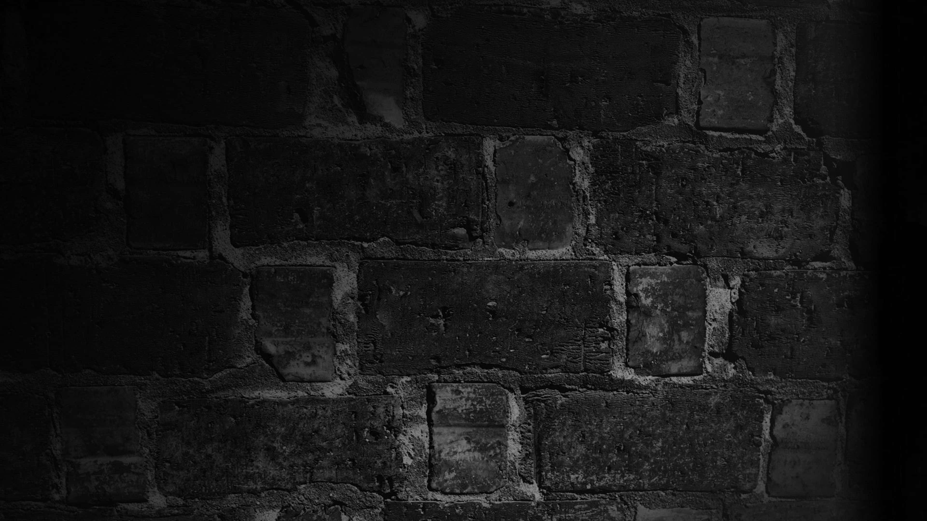 Dark Wall 桌布 壁紙 — 一個特寫鏡頭，展示深陰影中風化的磚牆，微妙的灰色高光揭示了粗糙的紋理和陳舊的砂漿。