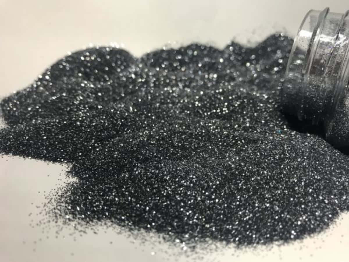 Black Powder 桌布 壁紙 — 一個特寫鏡頭，閃亮的黑色閃粉從透明罐子灑落到白色表面上。