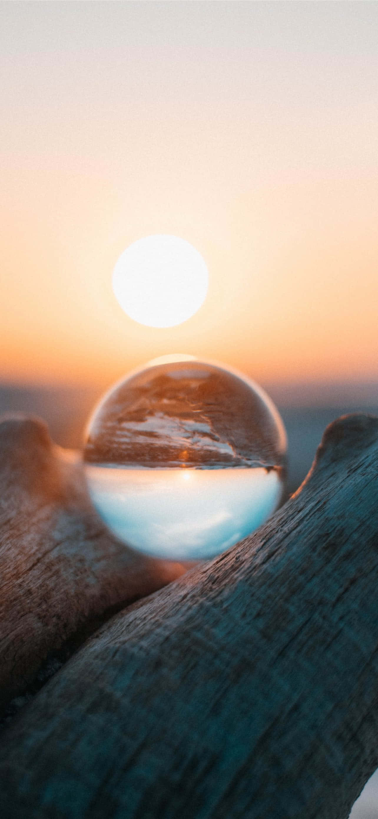 Beautiful Photography 桌布 壁紙 — 一個玻璃球放在風化的浮木上，反射出水面上閃耀的夕陽。