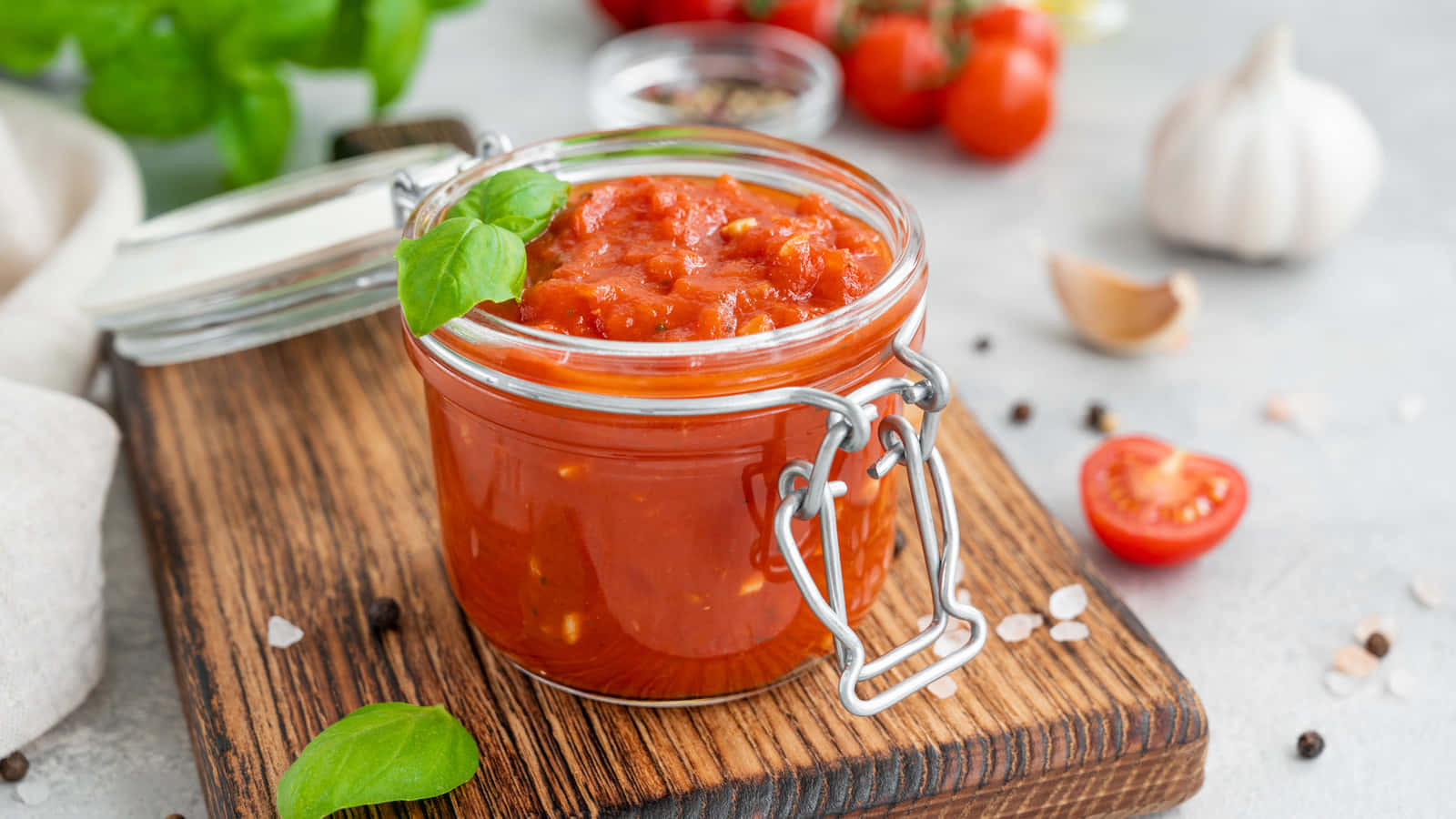Red Sauce 桌布 壁紙 — 一個玻璃瓶裝滿鮮紅色自製番茄醬，放在木板上，周圍是新鮮羅勒、大蒜和車厘茄。