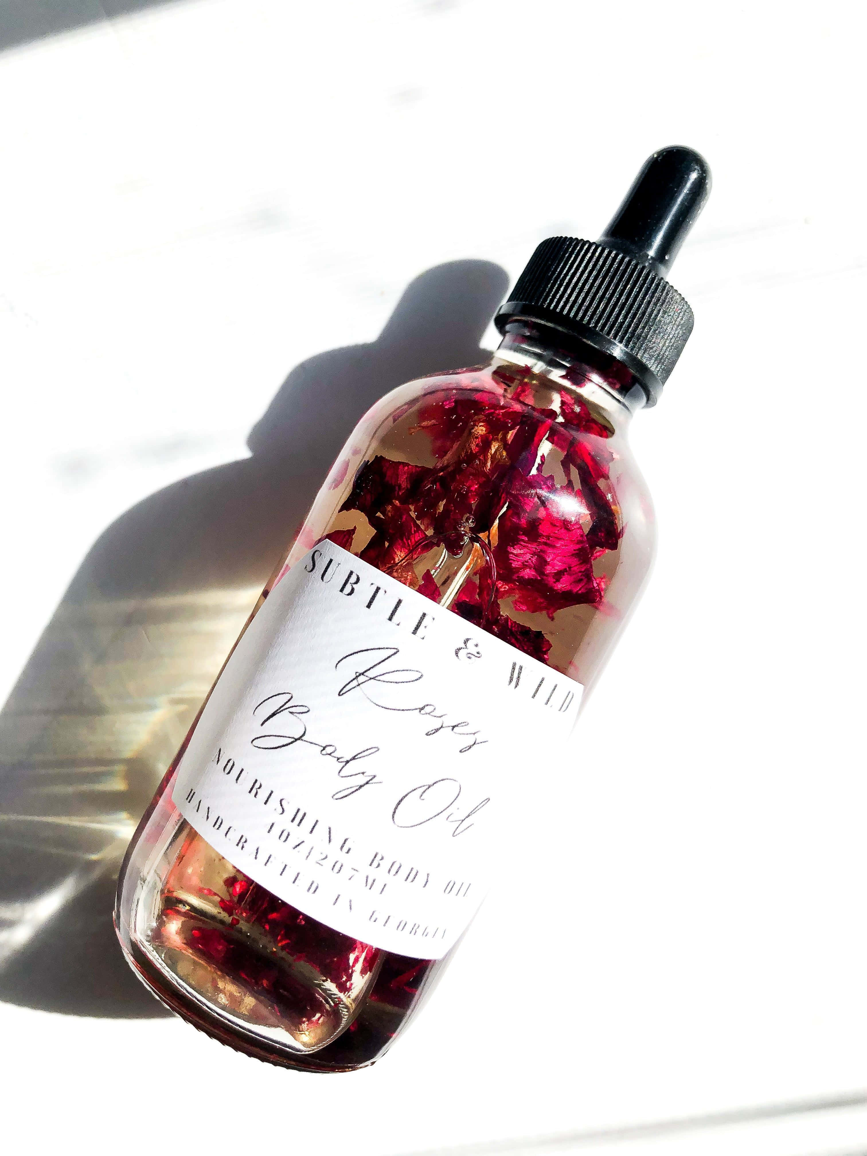 Rose Oil 桌布 壁紙 — 一個玻璃瓶裝玫瑰身體油，內有乾燥花瓣，在明亮的白色表面上投下清晰的陰影。
