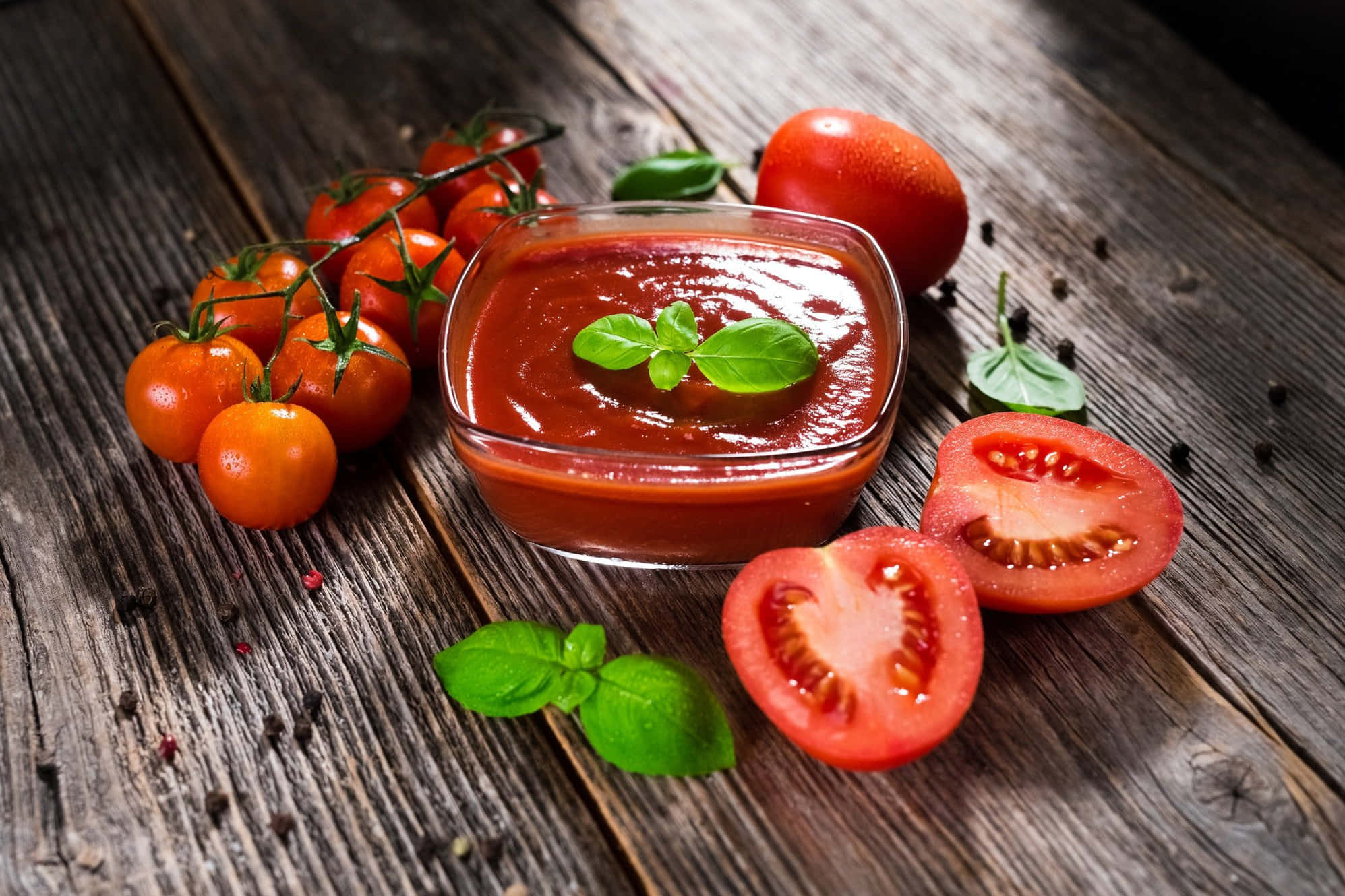 Red Sauce 桌布 壁紙 — 一個玻璃碗盛載著濃郁的紅色番茄醬，上面點綴著羅勒葉，旁邊放著新鮮的車厘茄和切片番茄，置於經風化的木質表面上。