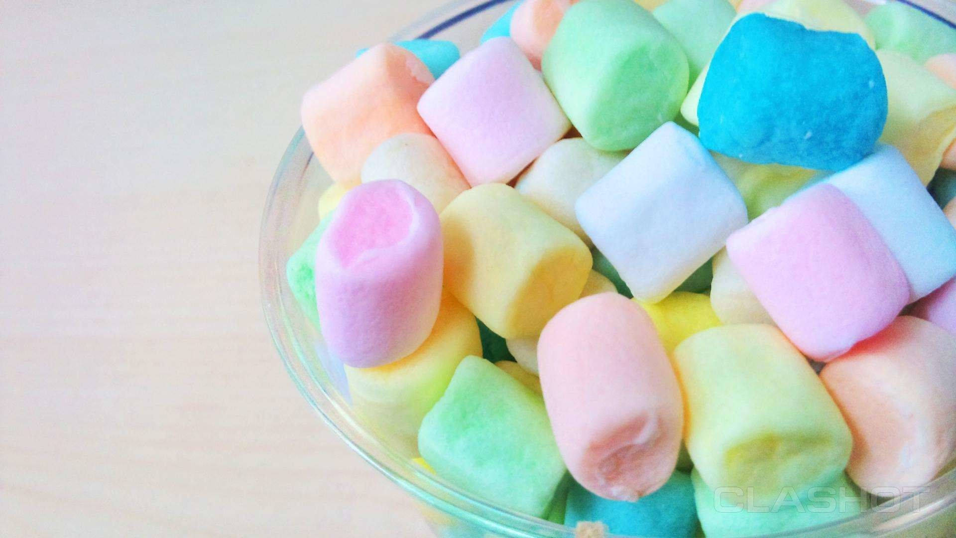 Marshmallow 桌布 壁紙 — 一個玻璃碗裝滿了粉彩色的 fluffy 棉花糖，放在淺色木質表面上。