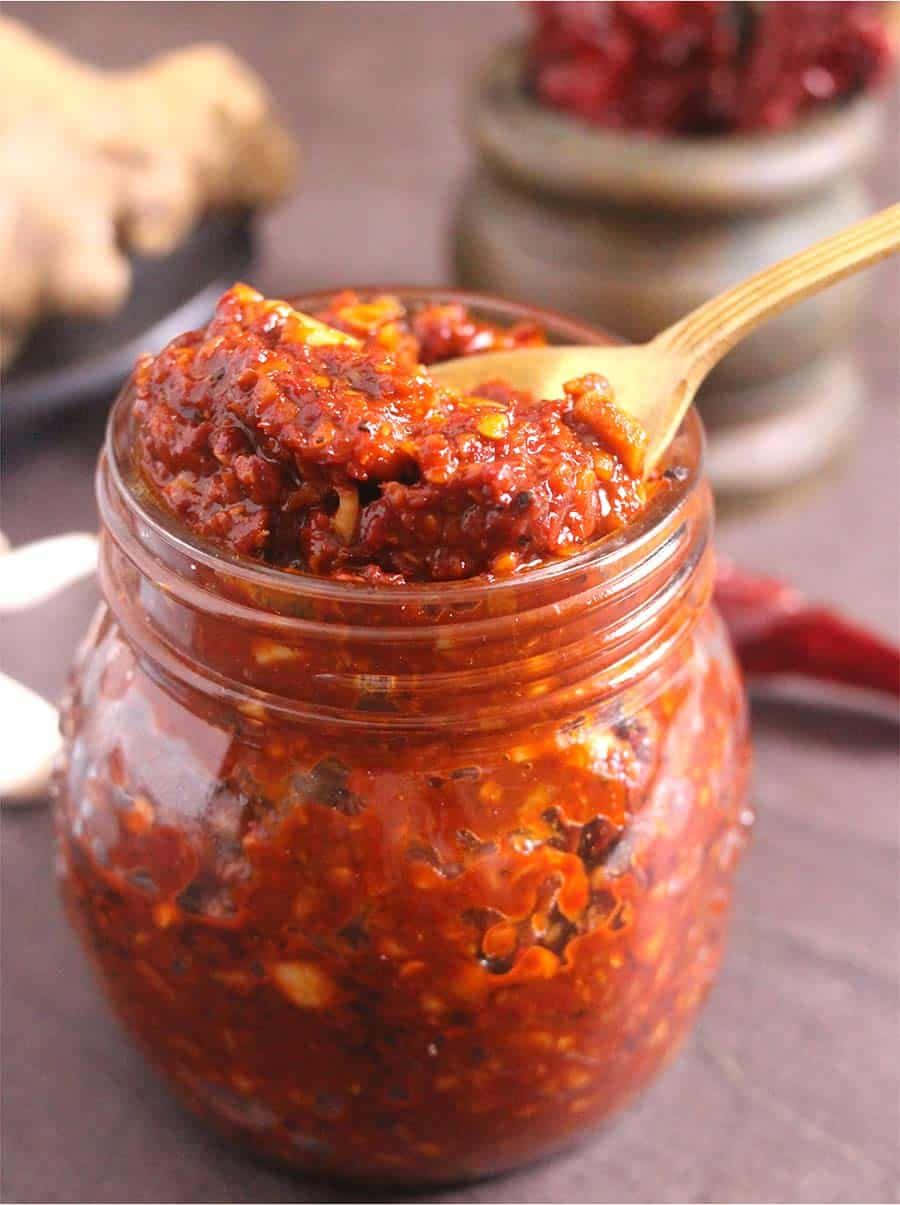 Szechuan Sauce 桌布 壁紙 — 一個玻璃罐裝滿了粗粒紅辣椒醬，上面放著一把木勺，背景是質樸的廚房。