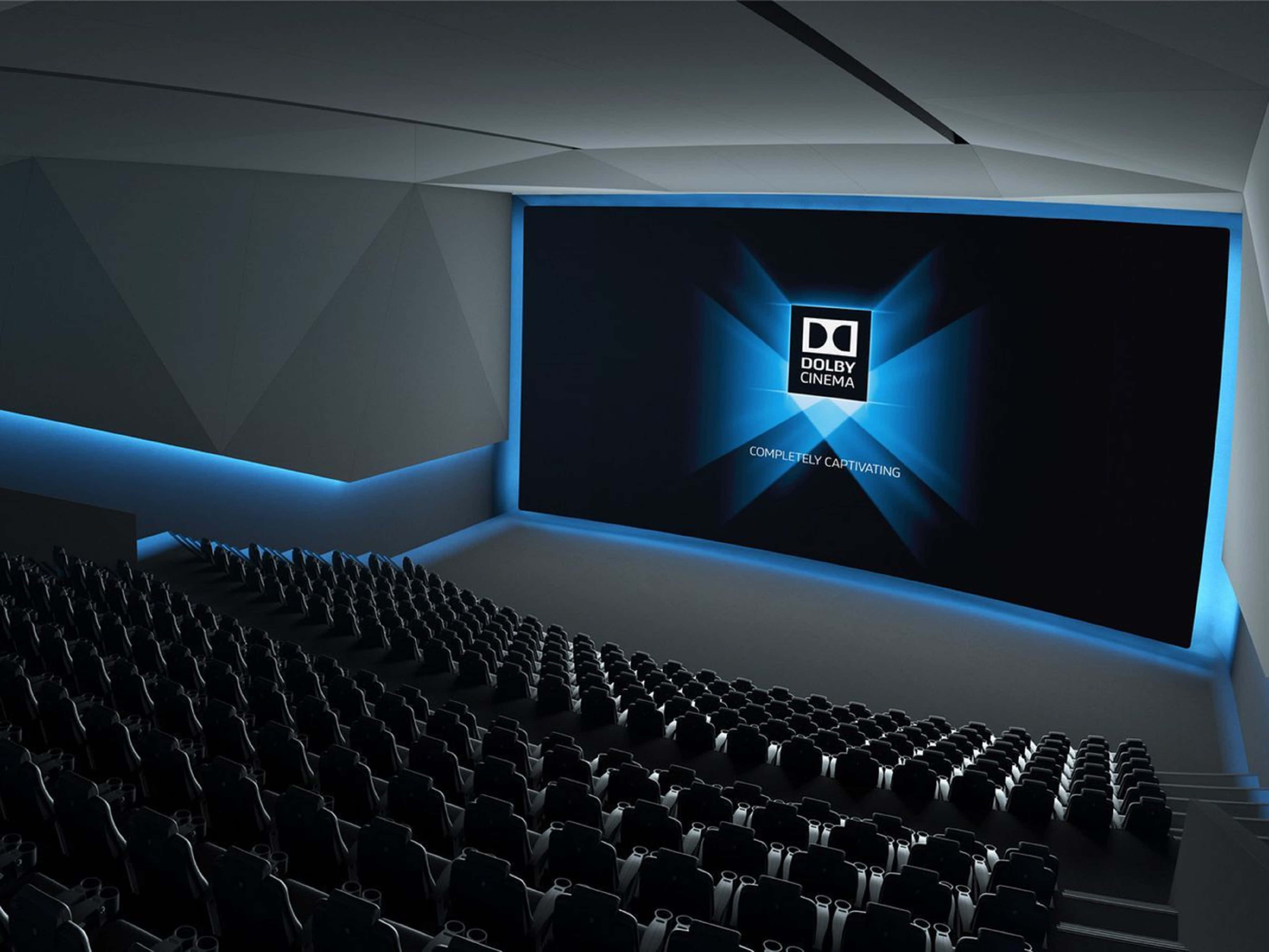 4K Dolby Vision 桌布 壁紙 — 一個現代化的影院禮堂，排列著黑色座椅，面向一個顯示Dolby Cinema標誌並被藍光照亮的大屏幕。