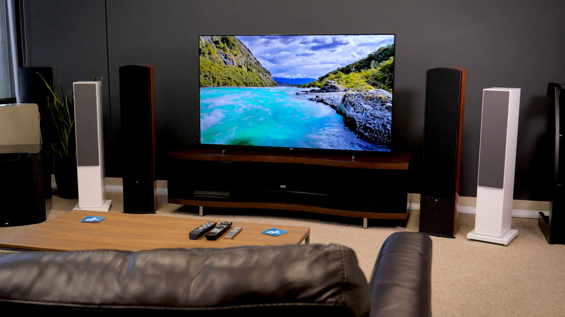 tv 桌布 壁紙 — 一個現代客廳，配備大型電視，顯示在戲劇性天空下，兩旁是茂密綠色懸崖的鮮豔藍綠色河流。