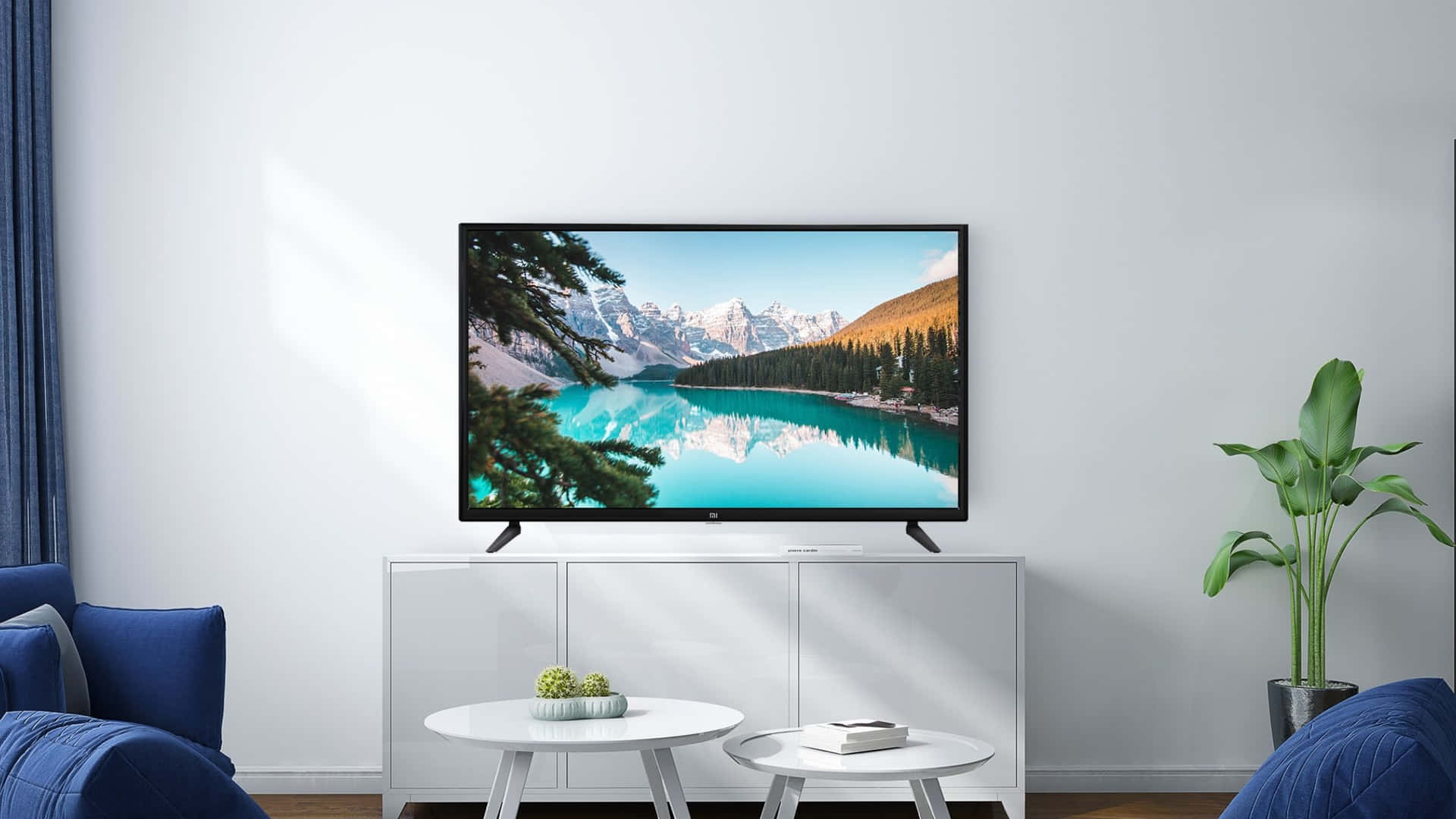 tv 桌布 壁紙 — 一個現代客廳，電視顯示著充滿活力的山湖景色，周圍環繞著白雪覆蓋的山峰和秋天的樹木。