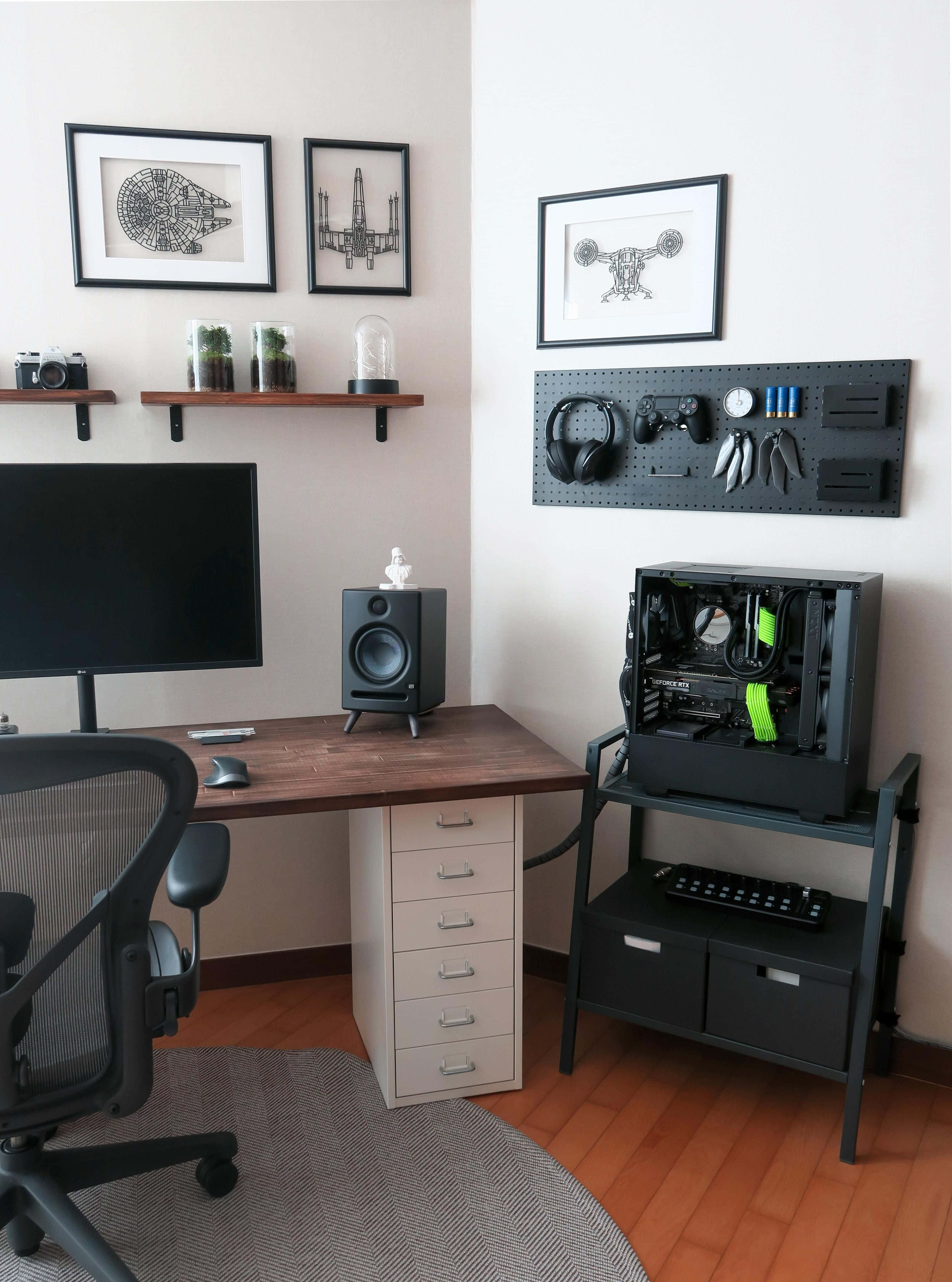 Gaming Accessories 桌布 壁紙 — 一個現代家居辦公室，配有木桌、黑色電競椅和金屬支架上的開放式PC機箱，周圍環繞著裱框的星際大戰藝術品和浮動層架。