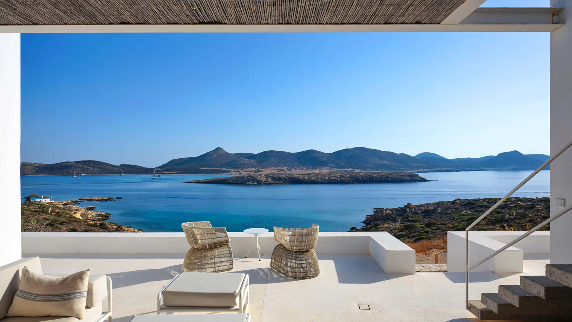 Greek Beach 桌布 壁紙 — 一個現代白色露台俯瞰著碧綠的海水和遠處的山丘，天空湛藍清澈。