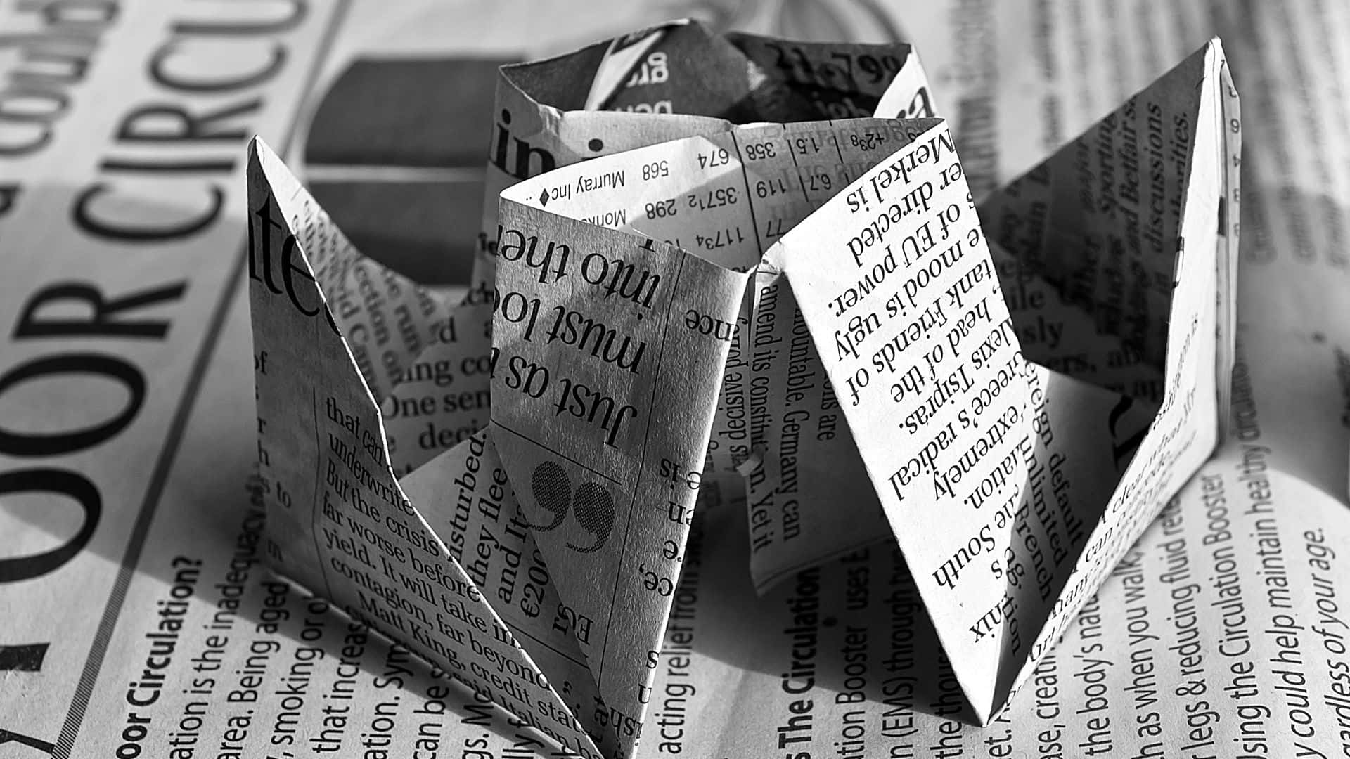 Black And White Newspaper 桌布 壁紙 — 一個用報紙文字製成的黑白摺紙算命器，放在模糊的報紙背景上。
