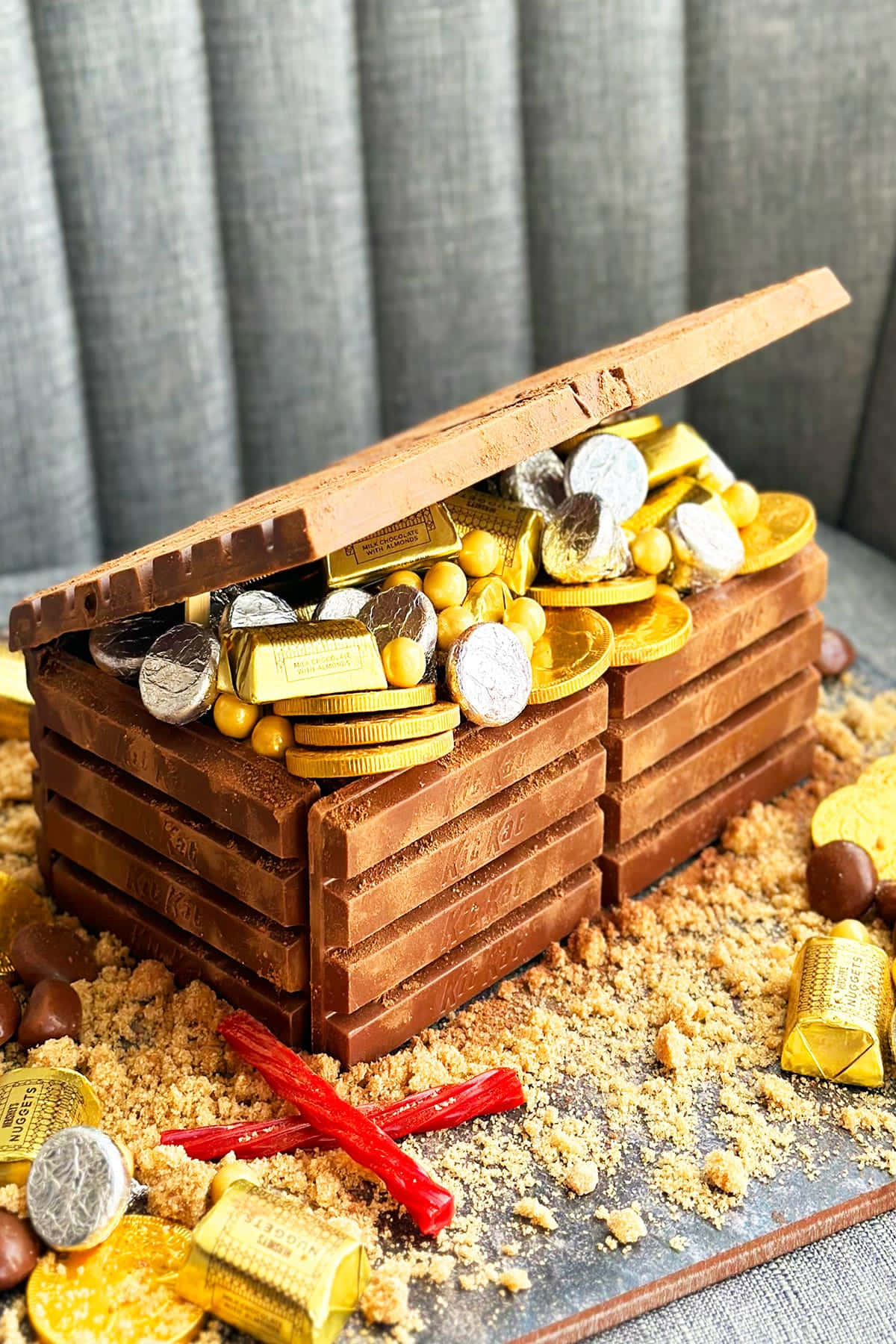 Treasure 桌布 壁紙 — 一個用朱古力棒製成的寶箱，在沙地上溢出糖果金幣和金色包裝紙。