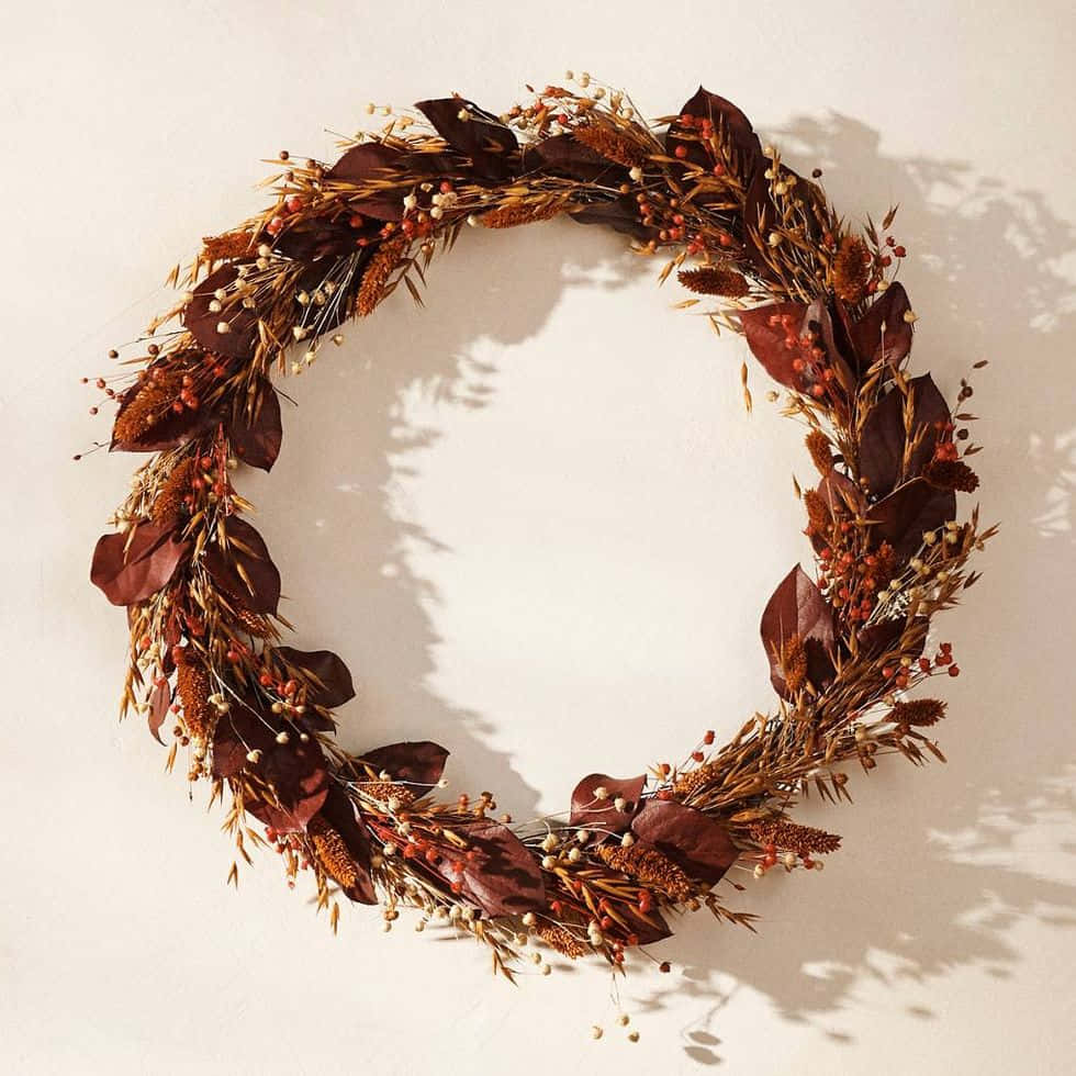 Fall Wreath 桌布 壁紙 — 一個由乾燥樹葉、草和漿果製成的鄉村風格秋季花環掛在素牆上，投下柔和陰影。