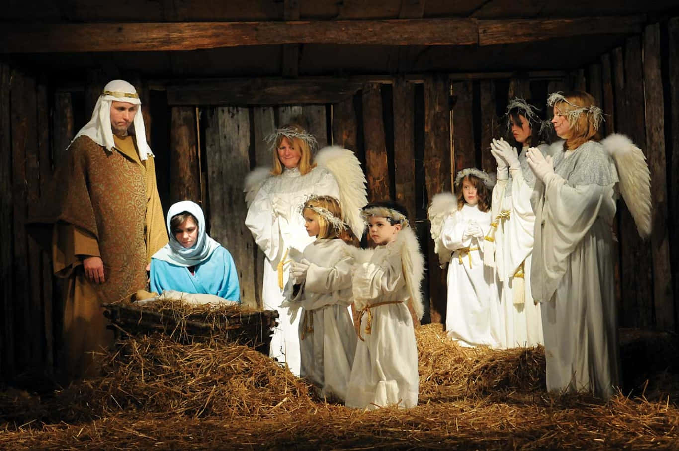 Nativity 桌布 壁紙 — 一個由演員扮演瑪利亞、約瑟和天使的耶穌誕生場景，位於一個有乾草的質樸木製馬廄中。
