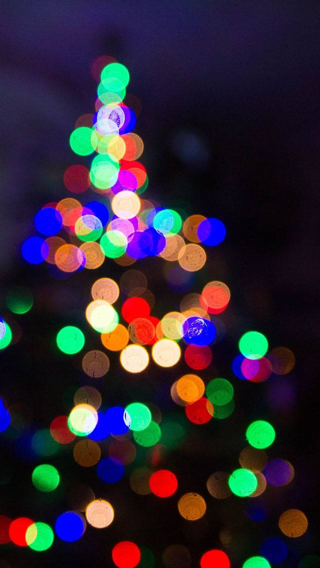Bokeh 桌布 壁紙 — 一個由發光多色燈光組成的節日散景聖誕樹，背景是黑暗的夜空。