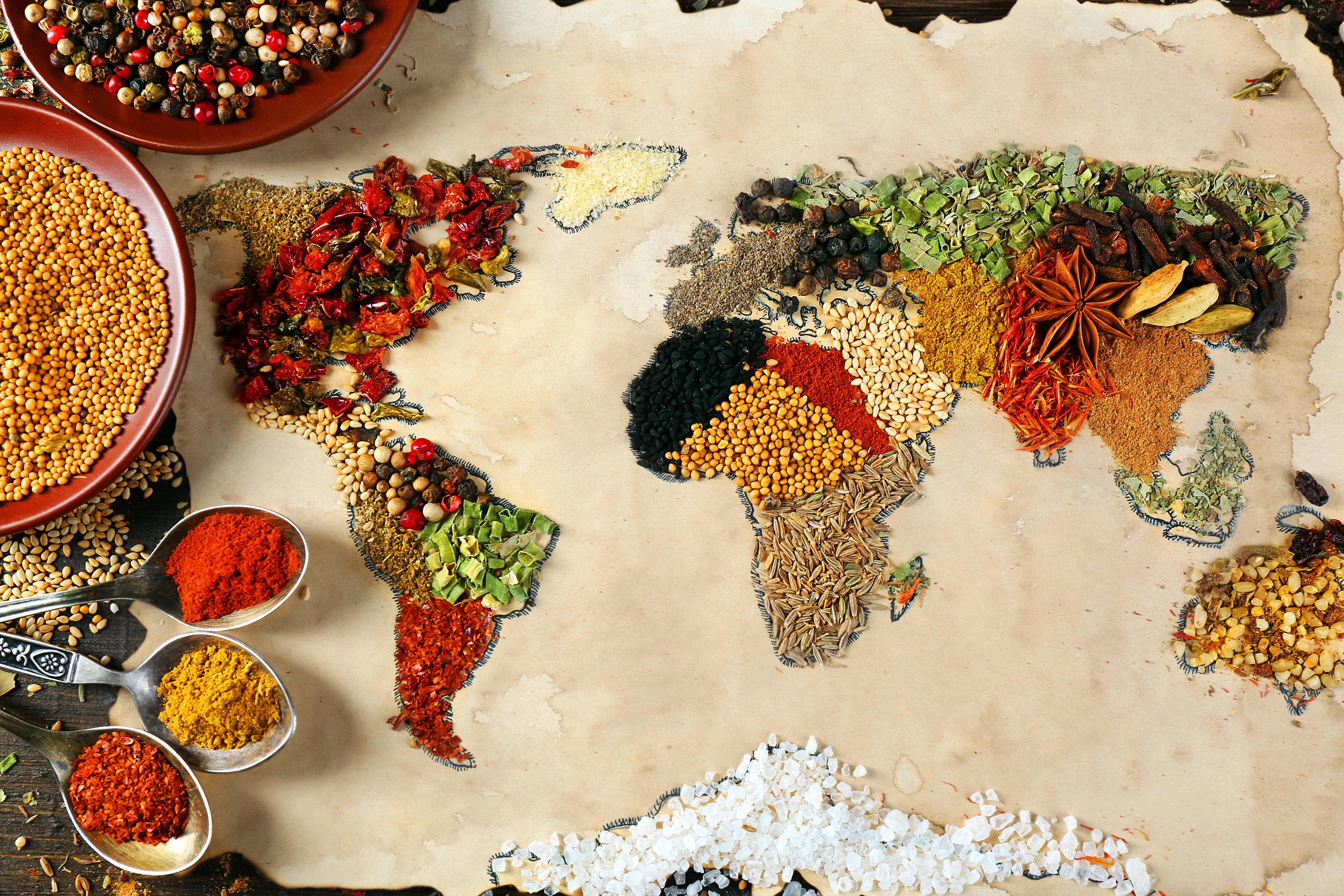 世界地圖 桌布 壁紙 — 一個由鮮豔香料和香草製成的世界地圖，排列在羊皮紙上，附近有碗和勺子盛放調味料。