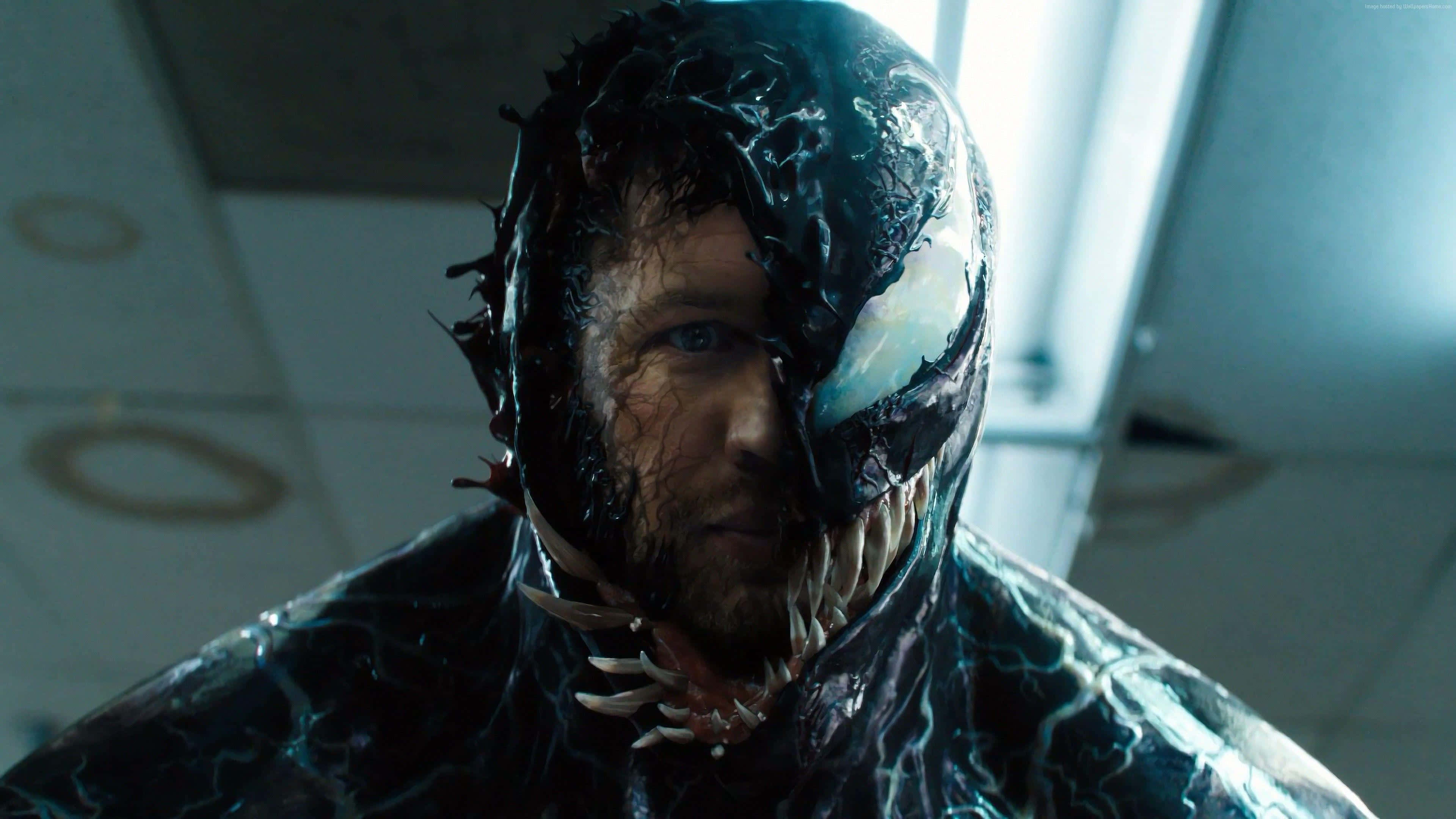 Tom Hardy Venom 桌布 壁紙 — 一個男人半變身成黑色共生體毒液的特寫，露出尖牙和發光的白色眼睛，身處無菌室。