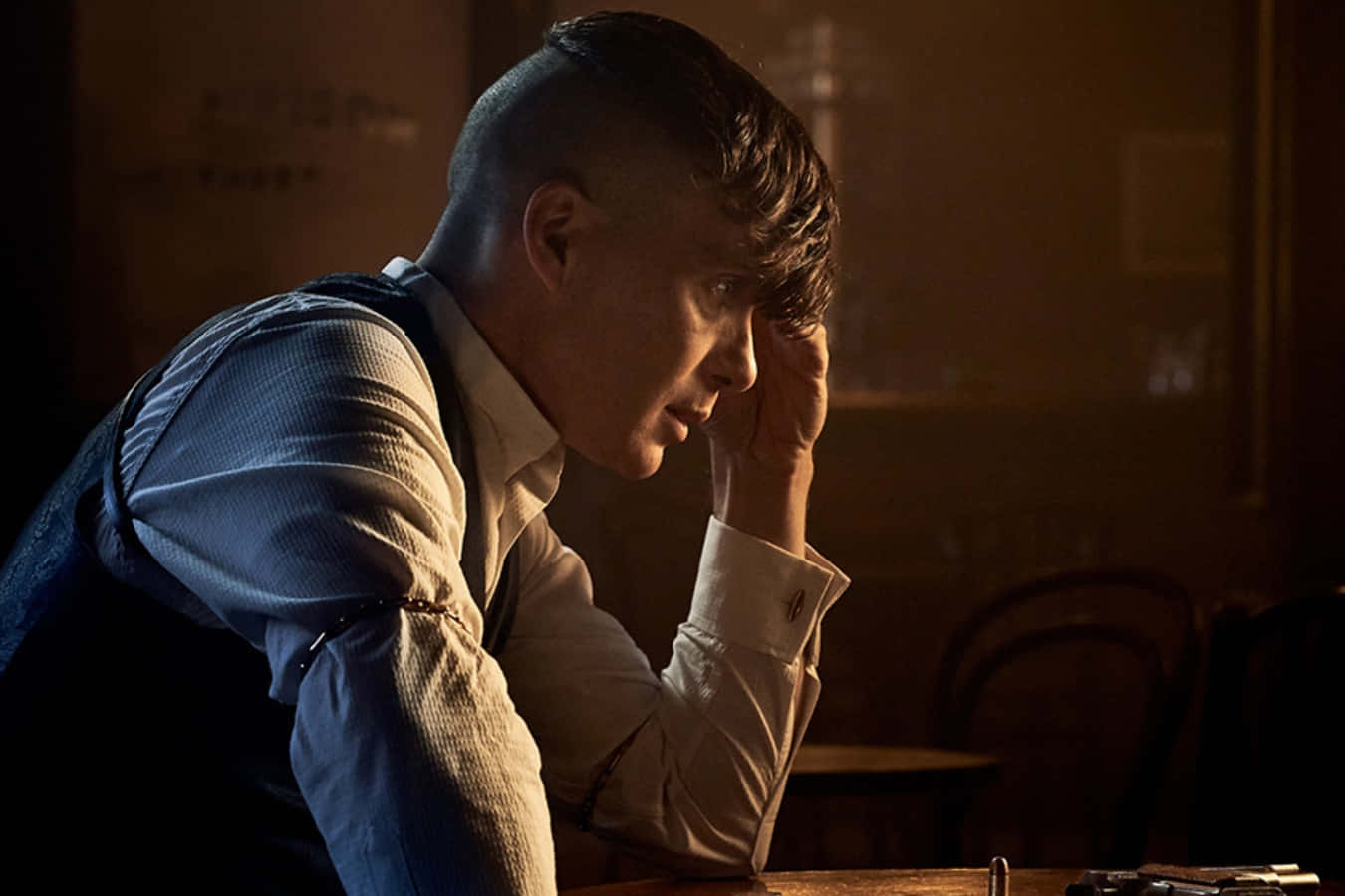 Peaky Blinders 桌布 壁紙 — 一個男人在昏暗的房間裏，用手托着頭，沐浴在溫暖的金色光芒中，傳達出深深的沉思。