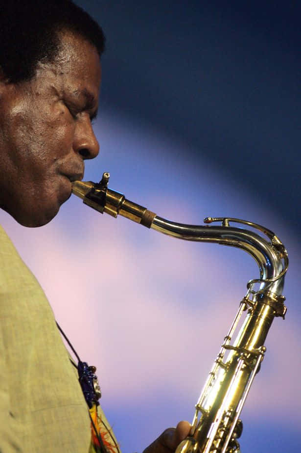 Wayne Shorter 桌布 壁紙 — 一個男人在柔和嘅紫藍色暮色天空下吹奏金色色士風嘅特寫。