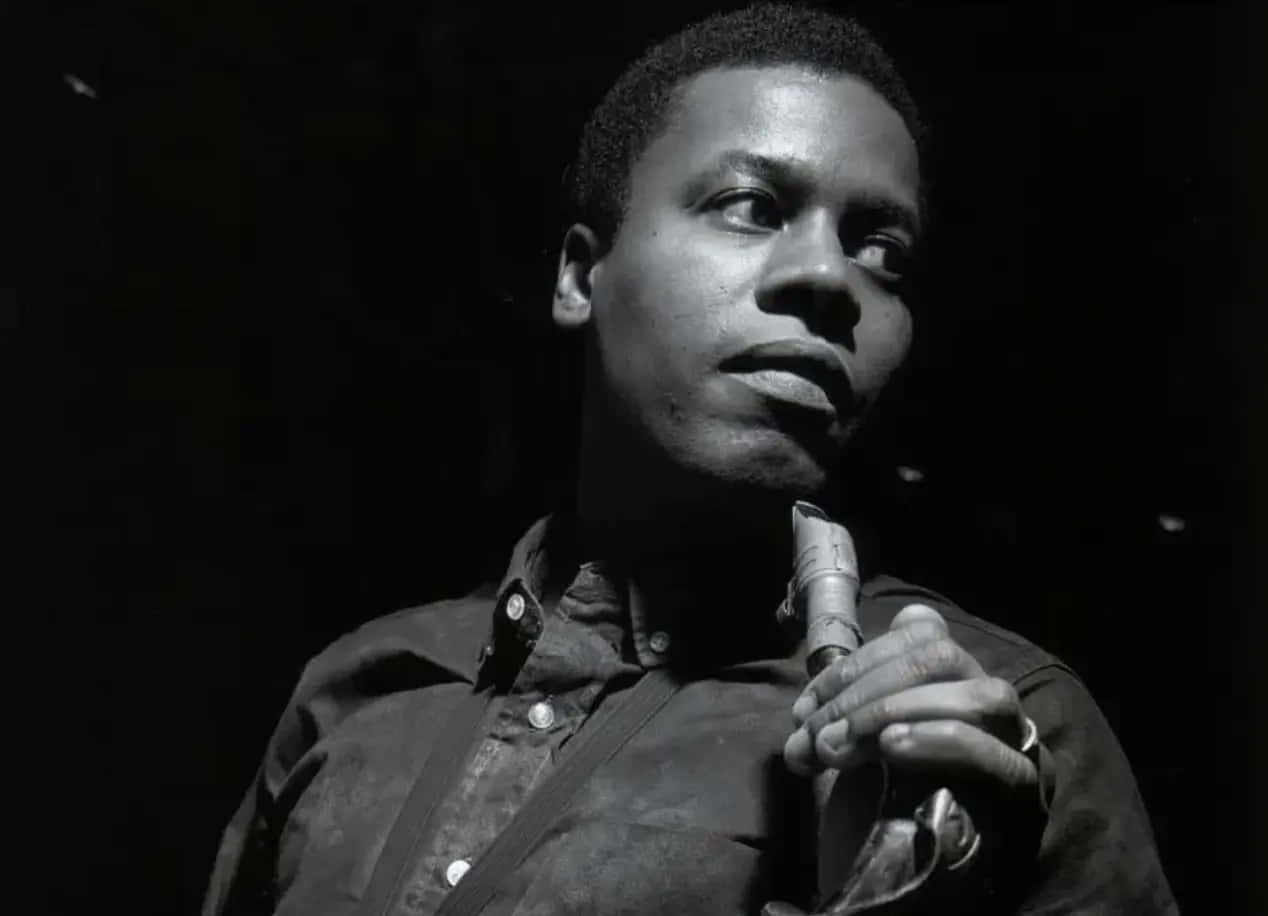 Wayne Shorter 桌布 壁紙 — 一個男人在黑暗背景中手持麥克風的黑白肖像，帶有戲劇性燈光。