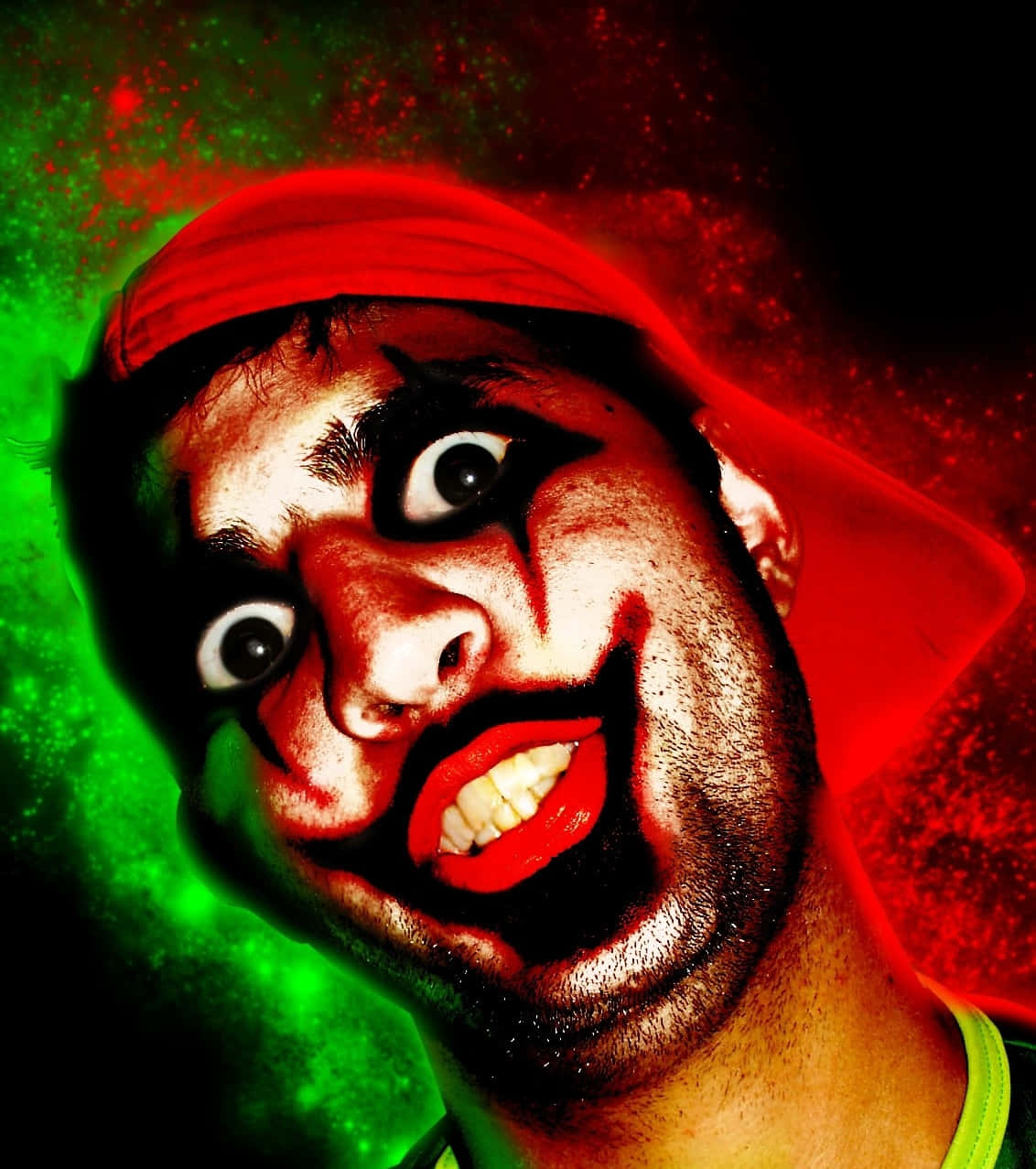 Freaky 桌布 壁紙 — 一個男人帶著誇張的小丑妝容和紅色頭巾，在充滿活力的綠色和紅色潑濺背景下強烈凝視。