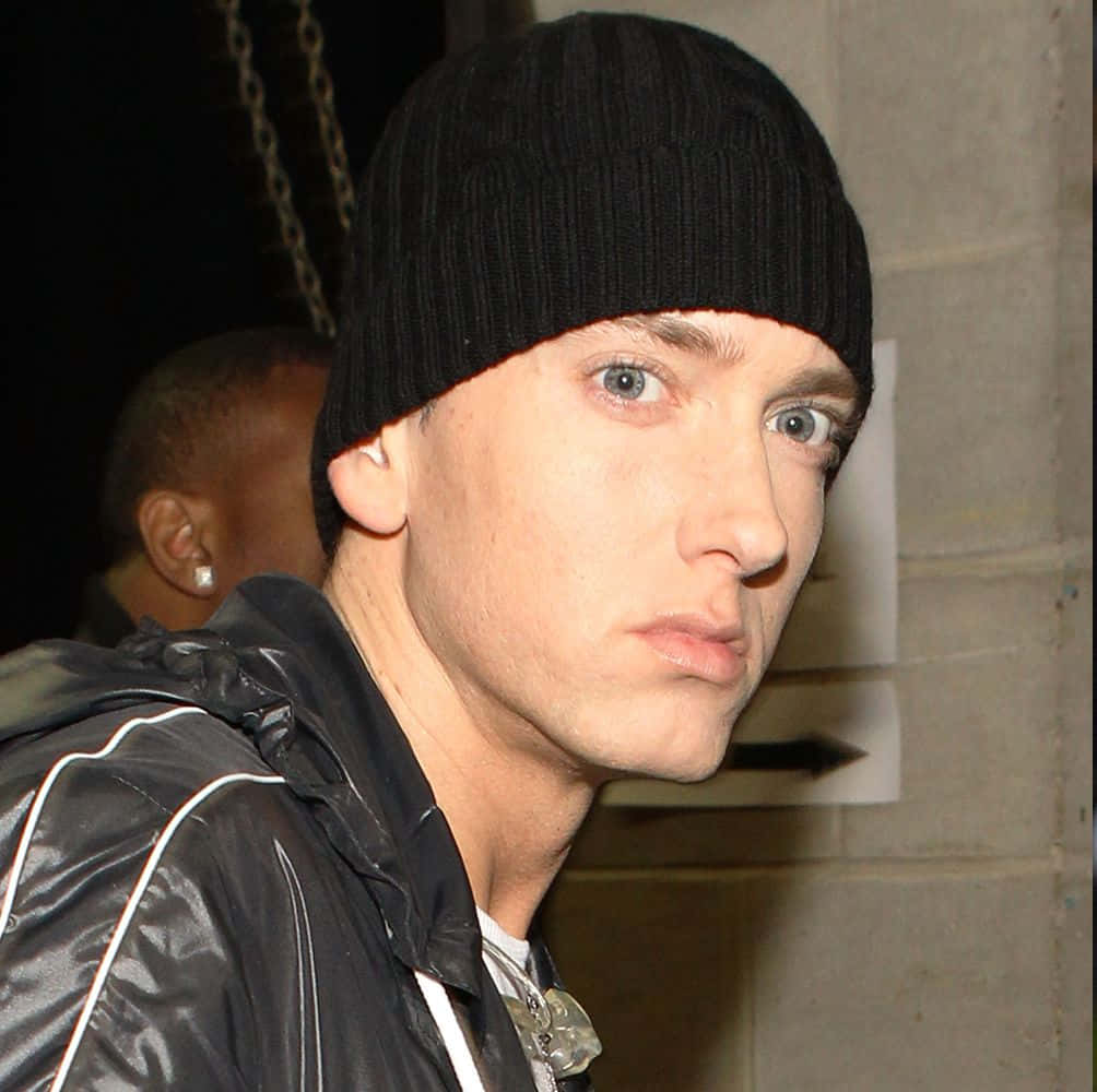 Eminem 桌布 壁紙 — 一個男人戴著黑色冷帽和閃亮黑色外套，在昏暗的城市環境中專注地看著相機的特寫。