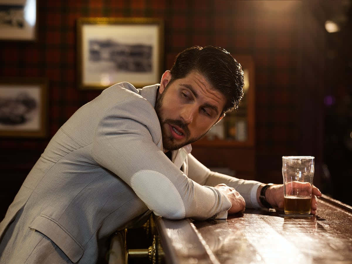 一個男人手拿啤酒，倚在吧檯邊 壁紙