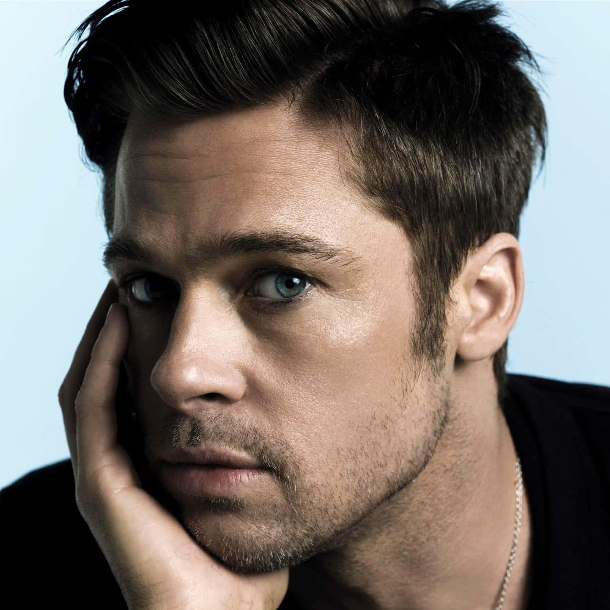 Brad Pitt 桌布 壁紙 — 一個男人的特寫肖像，他有著強烈的藍色眼睛，下巴擱在手上，背景是柔和的藍色。