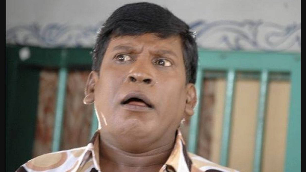 Vadivelu 桌布 壁紙 — 一個男人睜大眼睛、張開嘴巴，震驚地向上望，背景係有圖案嘅牆同綠色欄杆。