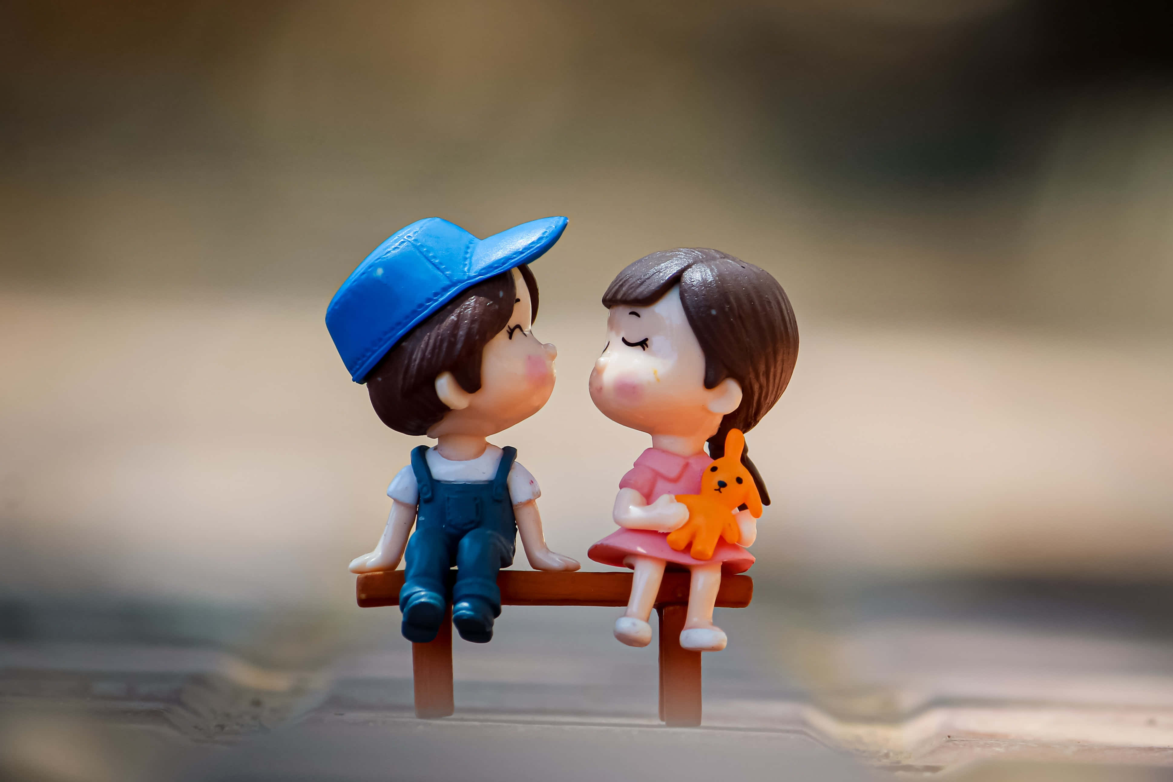 親吻 桌布 壁紙 — 一個男孩和一個女孩的微型人偶緊挨著坐在長椅上，在柔和自然光下分享溫馨時刻。