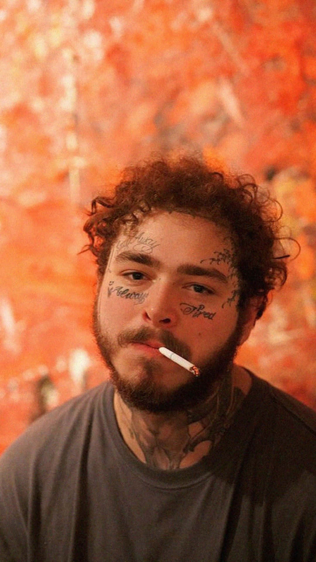 Post Malone 桌布 壁紙 — 一個留著捲髮、臉上紋身的男人，靠著火熱的橙色紋理牆壁抽煙。