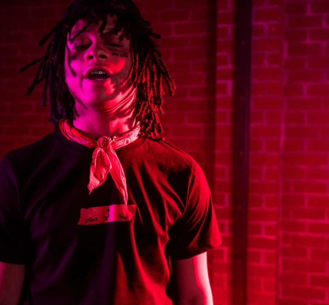 trippie redd 桌布 壁紙 — 一個留著辮子的人靠著磚牆站立，被強烈的紅光籠罩，閉著眼睛，嘴巴微微張開。