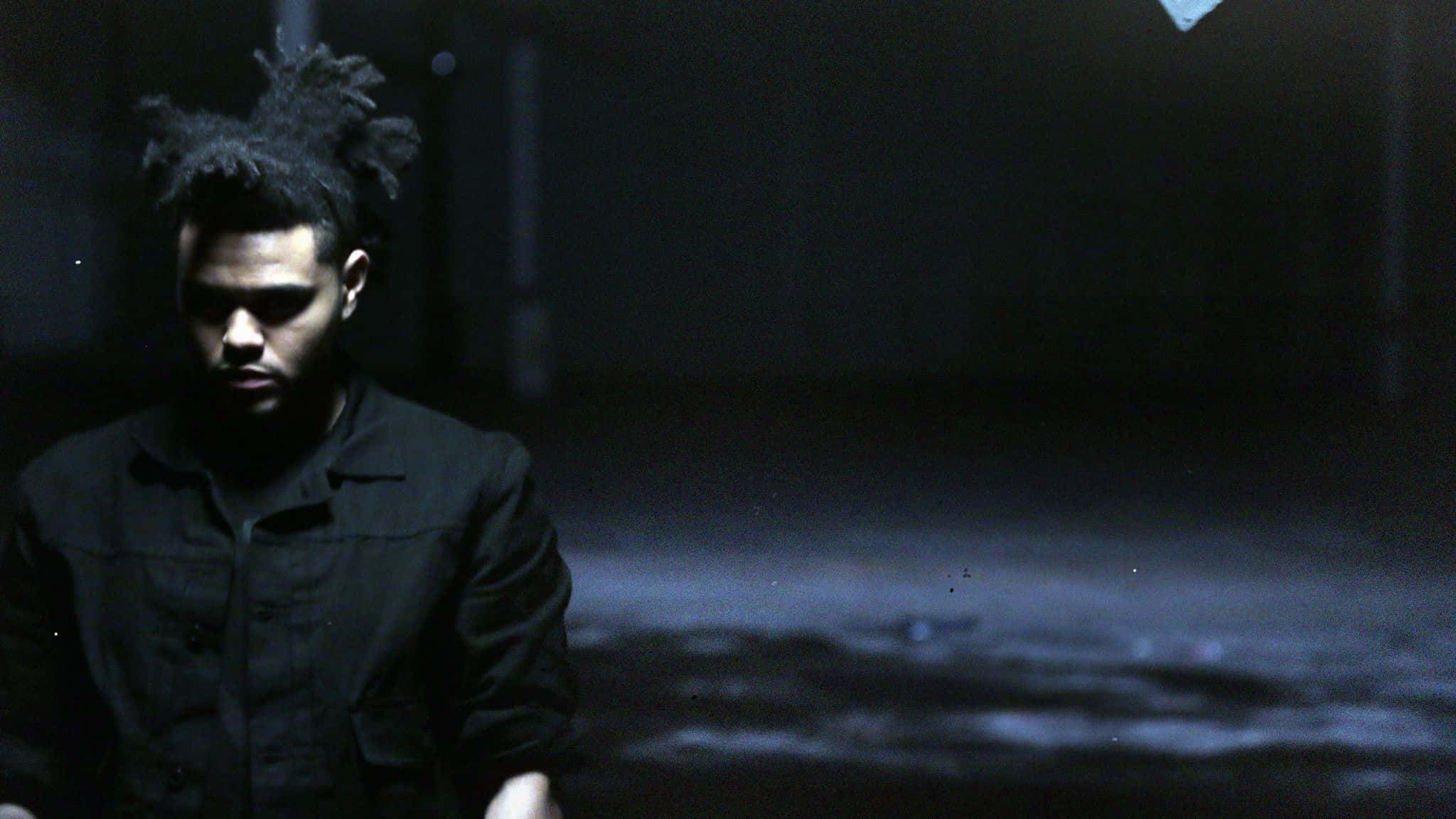 The Weeknd 桌布 壁紙 — 一個留著辮子頭的男人在夜晚昏暗的城市小巷中向下凝視，帶有憂鬱的藍色光芒。