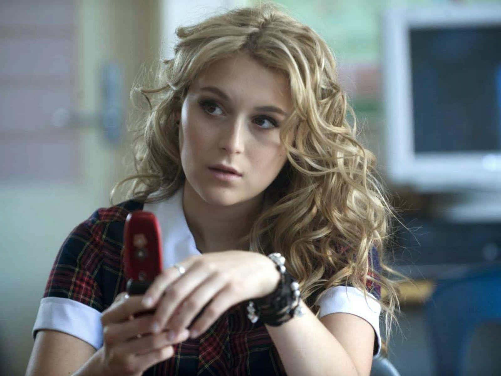 Alexa Penavega 桌布 壁紙 — 一個留著金色捲髮的少女在教室裡拿著一部紅色翻蓋手機。
