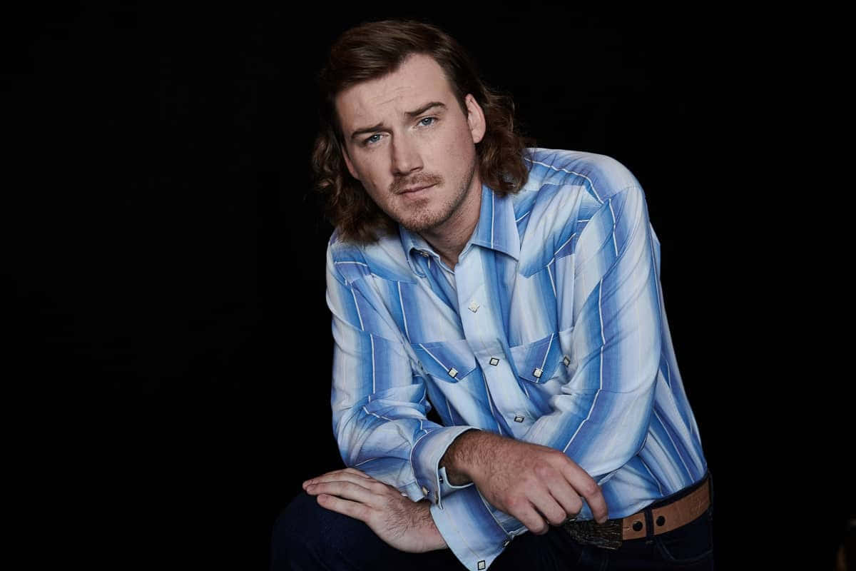 Morgan Wallen 桌布 壁紙 — 一個留著長棕髮和鬍鬚的男人，穿著藍色條紋襯衫，背景為黑色。