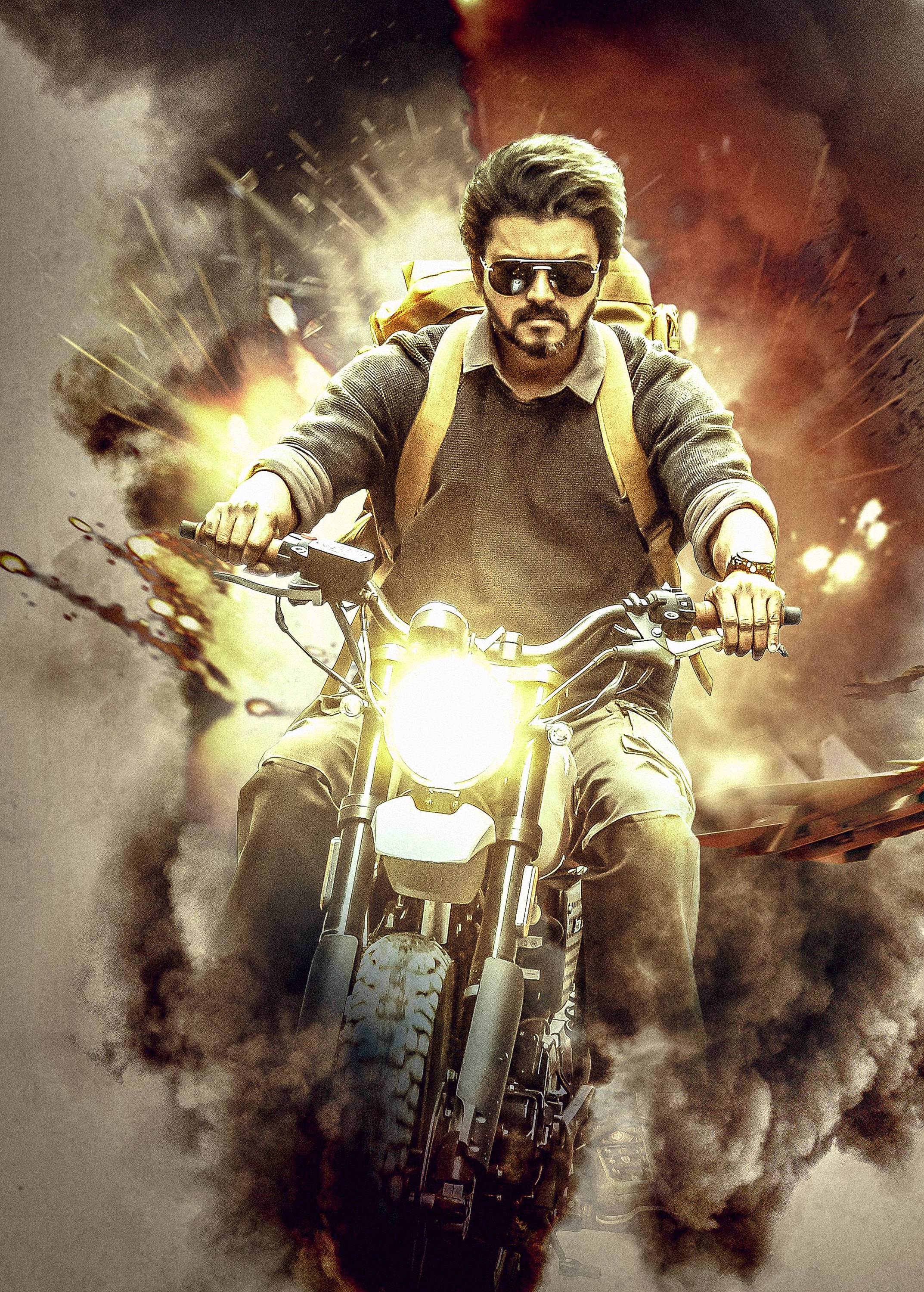 vijay HD 桌布 壁紙 — 一個留鬍子、戴太陽眼鏡的男人騎著電單車穿過爆炸，周圍充滿煙霧和火焰。
