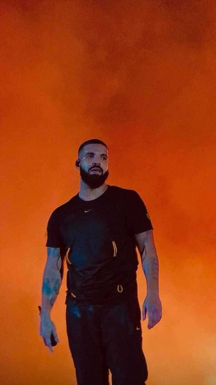 Drake 桌布 壁紙 — 一個留鬍子、有紋身的男人，自信地站在火橙色煙霧背景前，穿著黑色運動服。