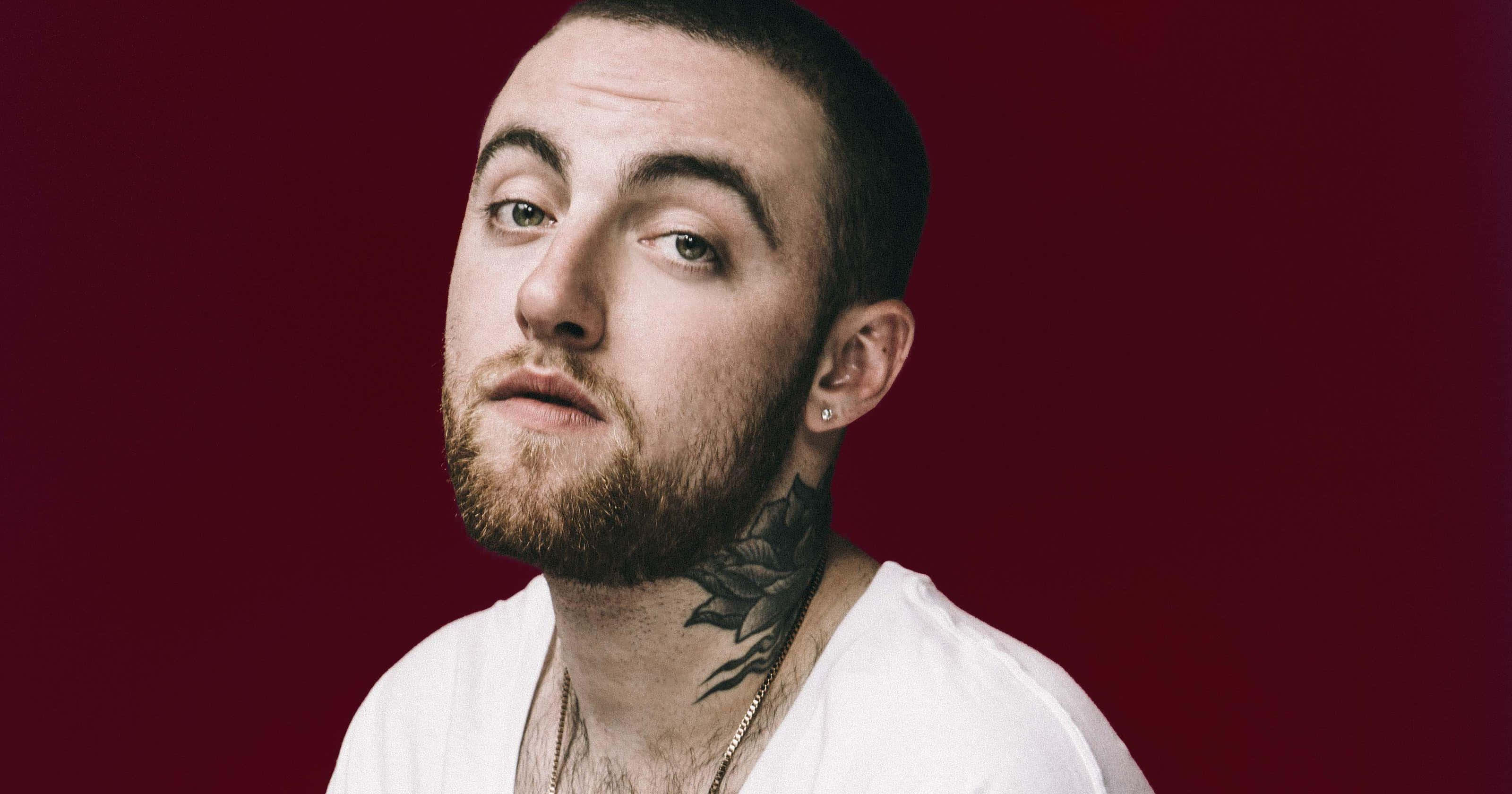 Mac Miller 桌布 壁紙 — 一個留鬍子、頸部有紋身的男人，在深紅色背景前凝視著。