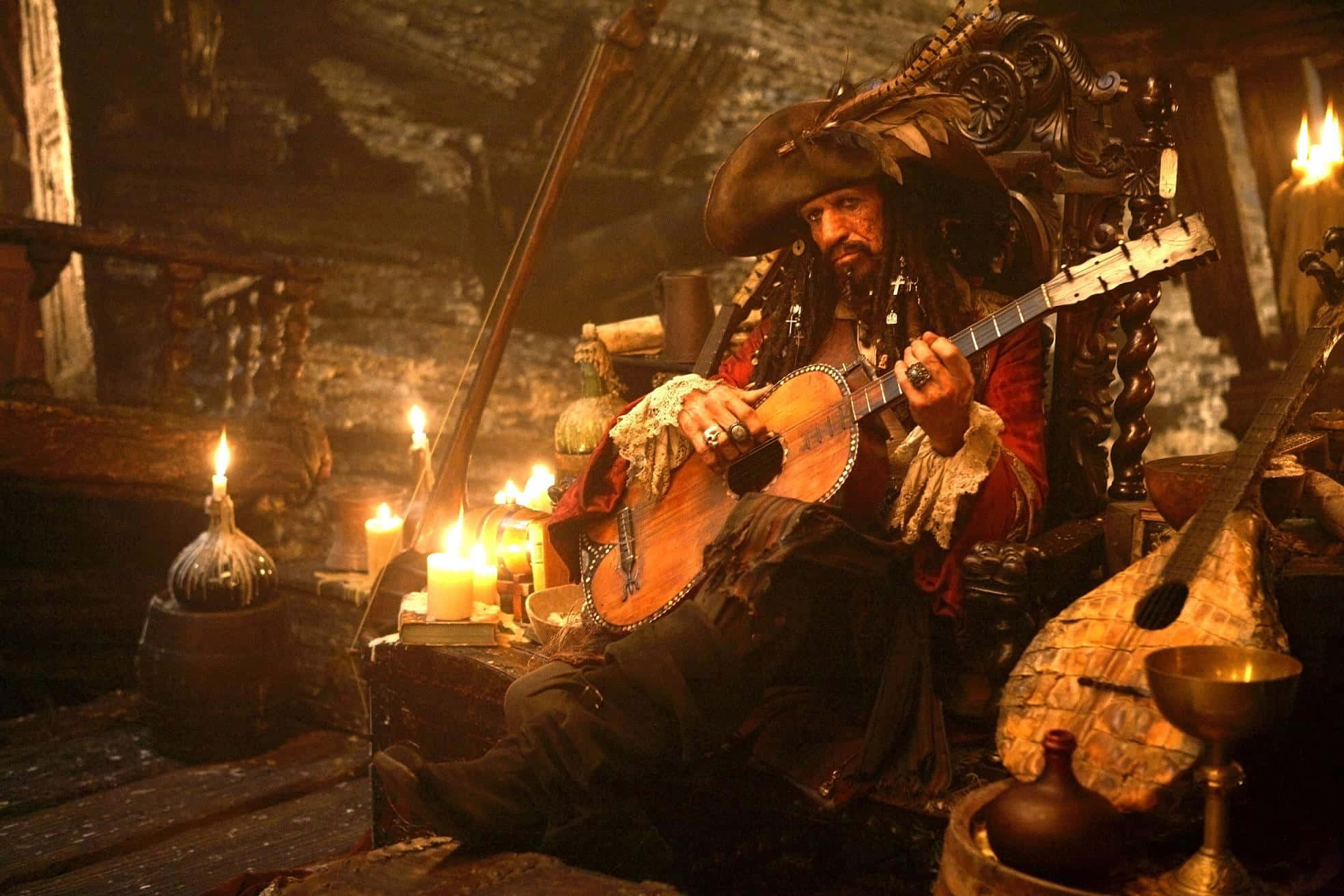 Pirates Of The Caribbean 桌布 壁紙 — 一個留鬍子戴帽子的海盜坐在類似王座的椅子上，在昏暗的木房間裏燭光下彈奏魯特琴。