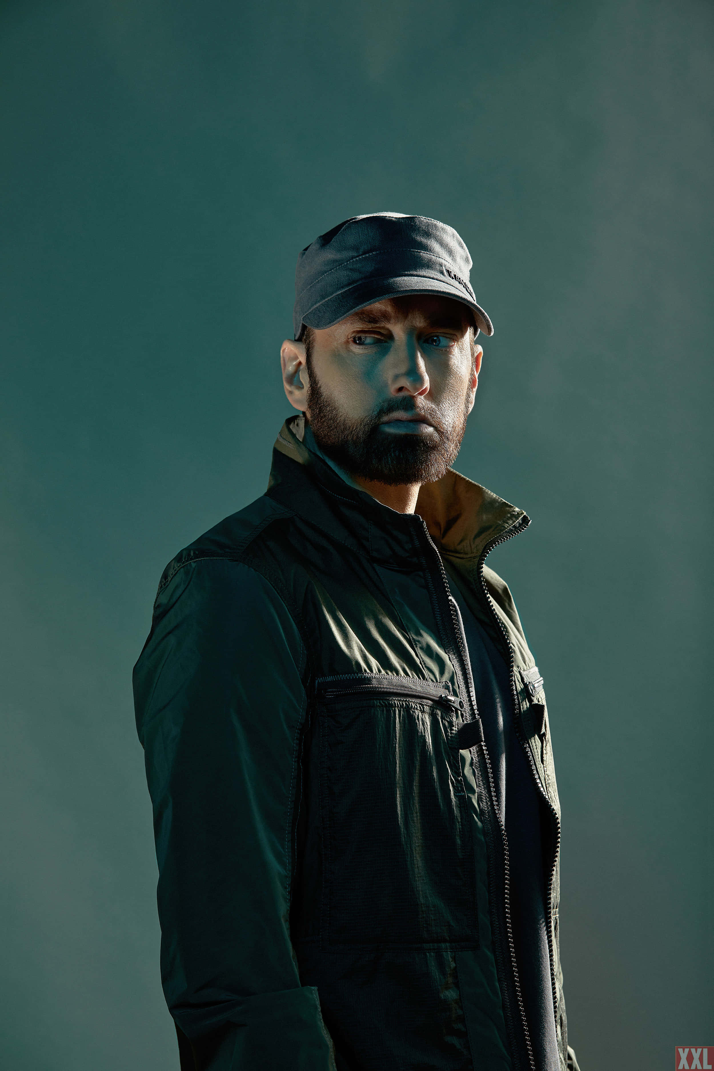 Eminem 桌布 壁紙 — 一個留鬍子戴帽子的男人，在戲劇性燈光下，對著充滿氛圍的藍綠色背景凝視。