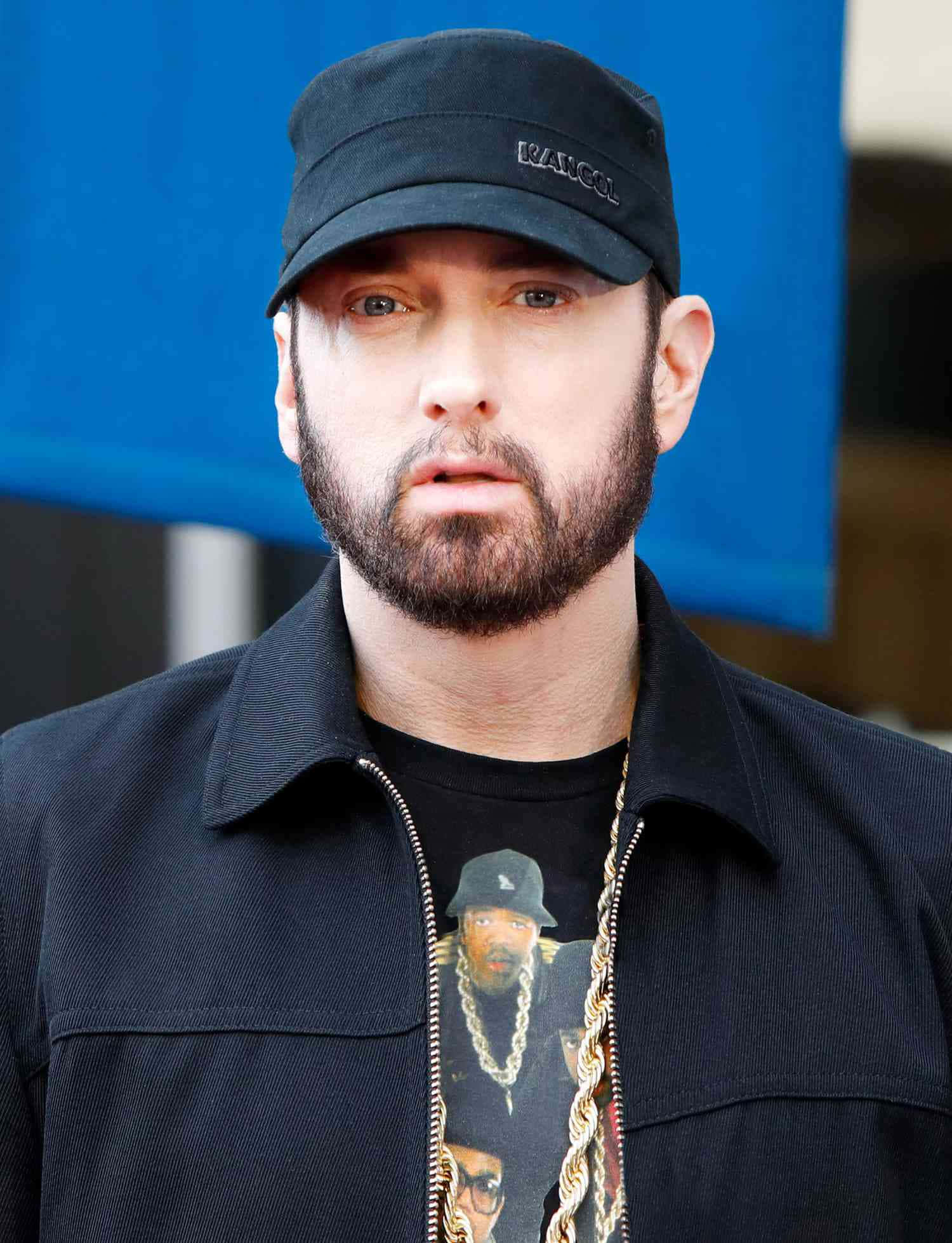 Eminem 桌布 壁紙 — 一個留鬍鬚、戴黑色帽子的男人，穿著黑色外套內搭有金色鏈條的圖案T恤，專注地凝視著。