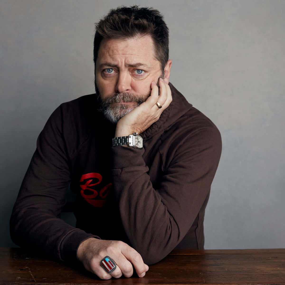 nick offerman 桌布 壁紙 — 一個留鬍鬚、藍眼睛嘅男人，將下巴擱喺手上，穿著啡色連帽衫同一個獨特嘅戒指。