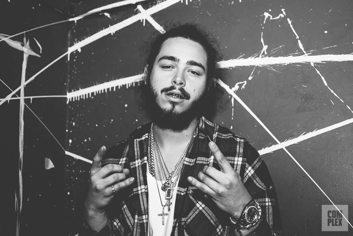 Post Malone 桌布 壁紙 — 一個留鬍鬚、身穿格仔恤衫的男人，在一個佈滿塗鴉的牆前做手勢，這是一幅粗獷的黑白肖像。